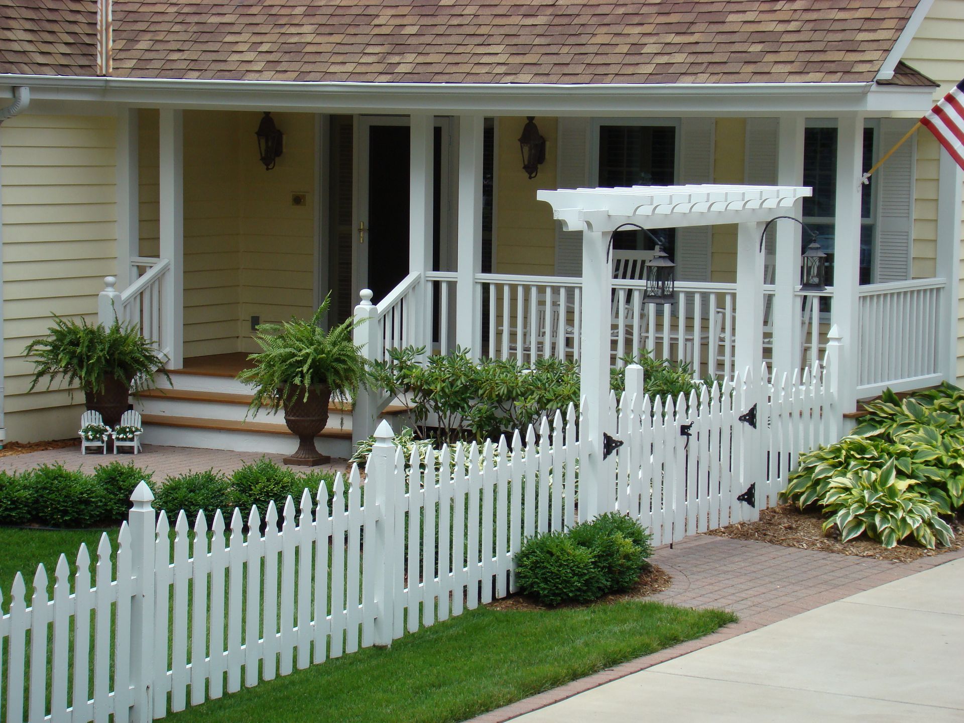 White picket fence and gate lead to a yellow house with a porch.