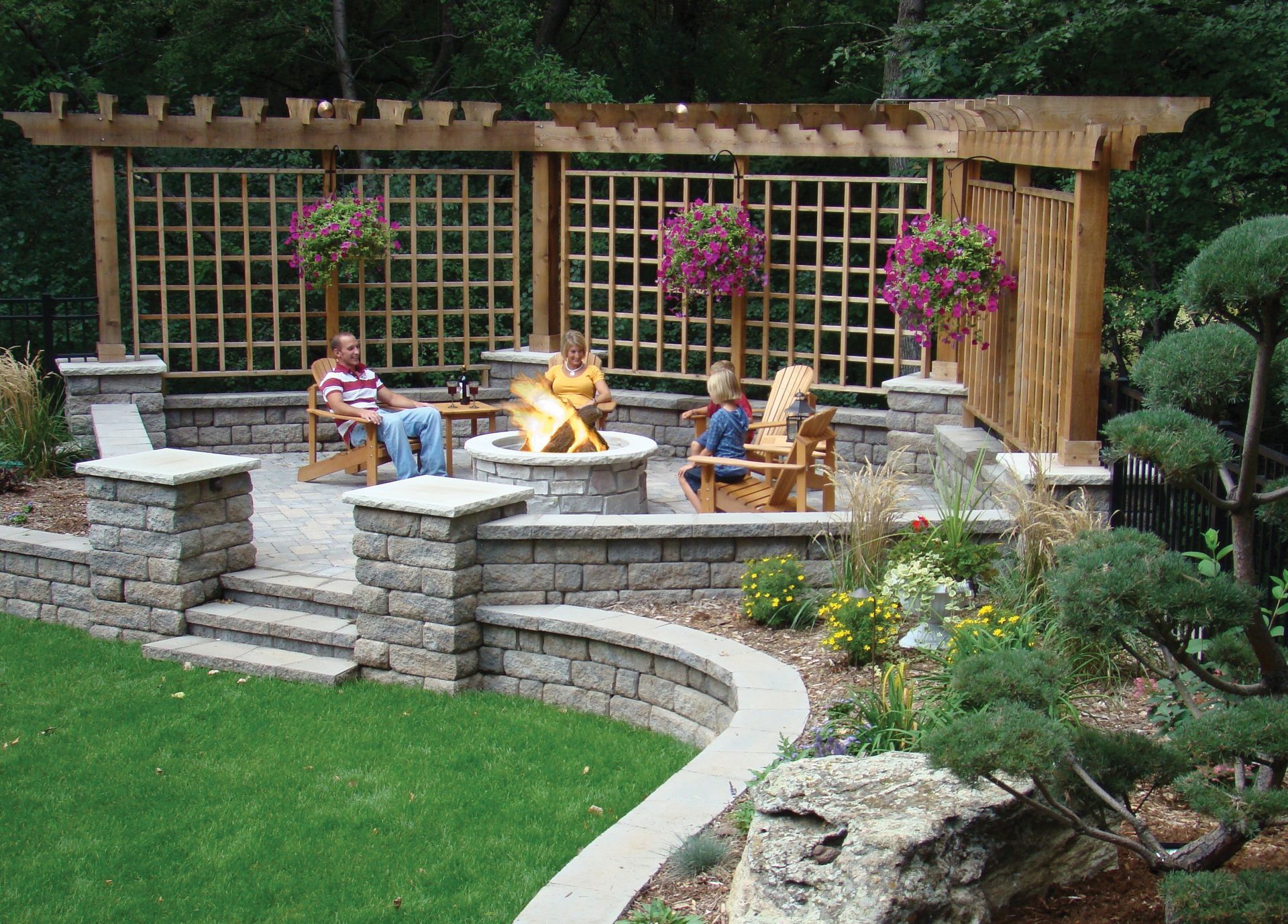 Stone patio with pergola, fire pit, and people relaxing outdoors.