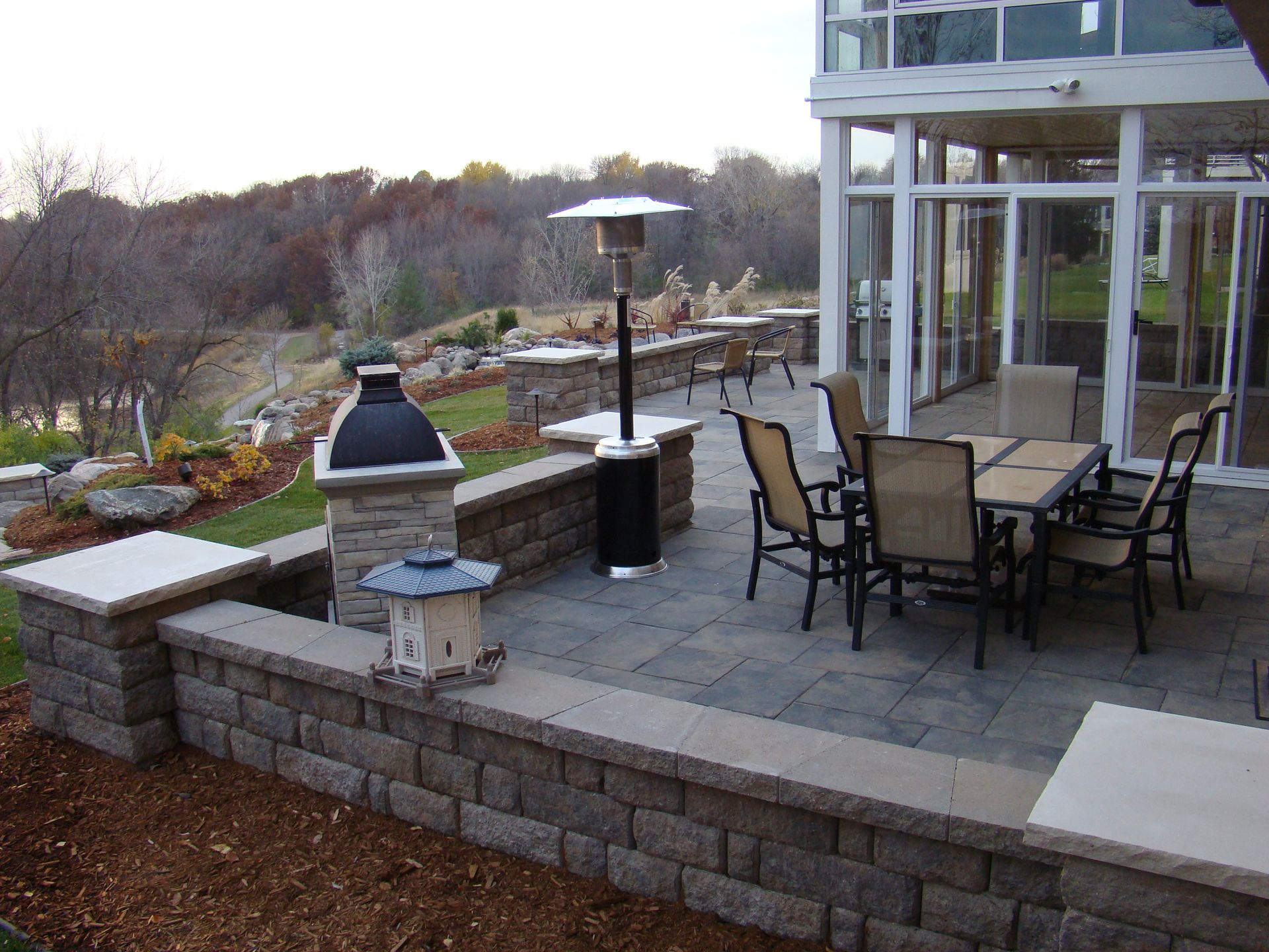 Patio with outdoor dining table and chairs, brick retaining walls, and scenic hillside view.