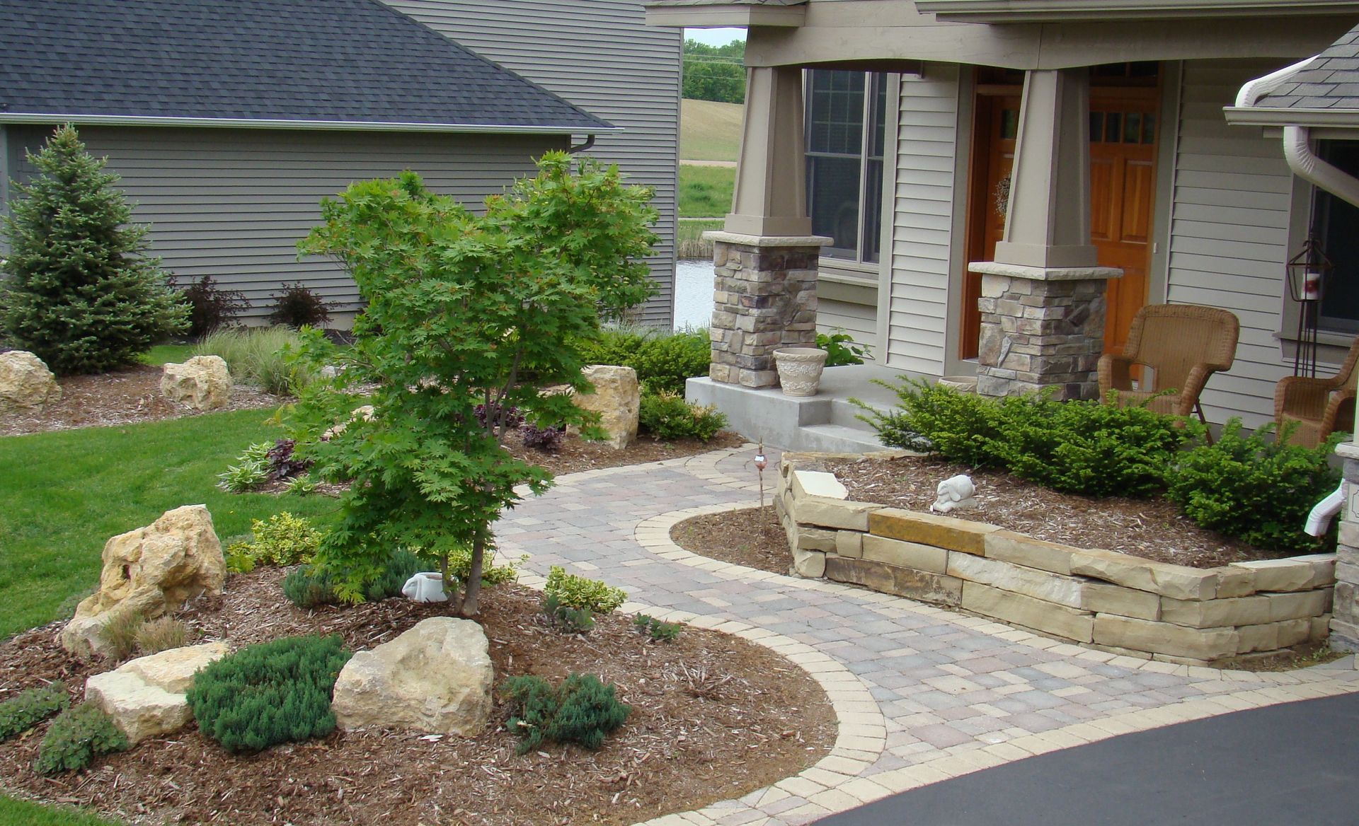 A landscaped front yard with a stone path, plants, and a house with a porch and pillars.