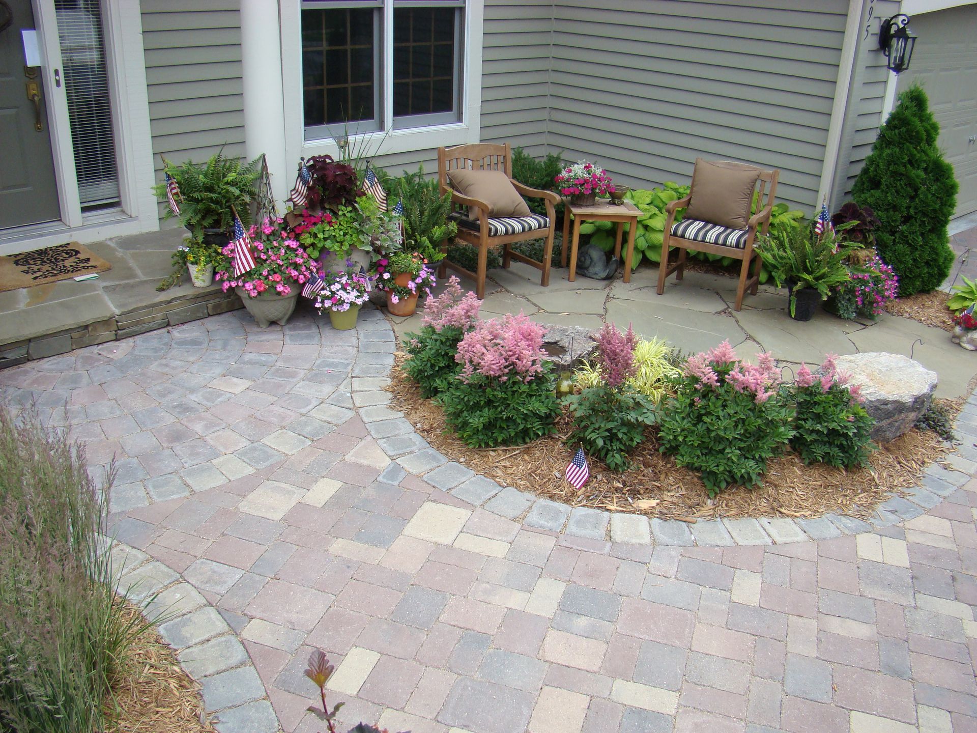 Stone patio with seating area, surrounded by potted flowers and a small garden bed.