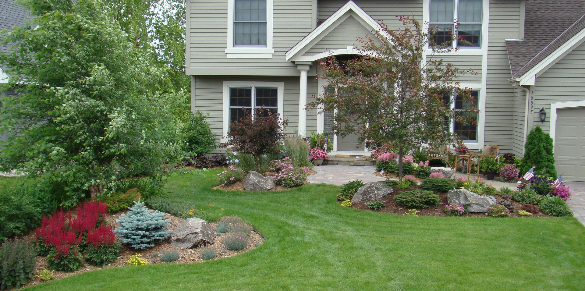 A house with a well-manicured lawn and a variety of colorful plants in the front yard.