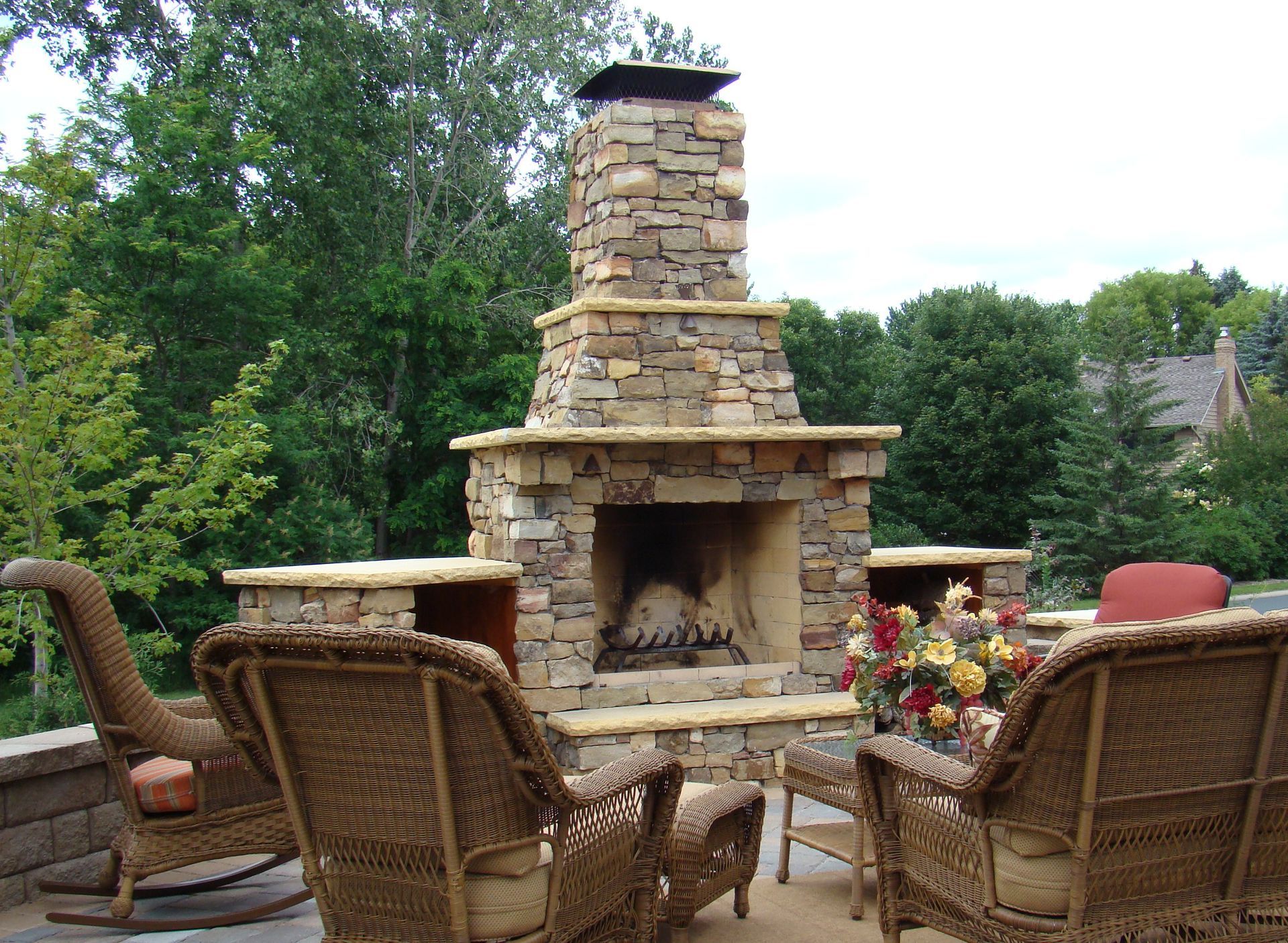 Outdoor stone fireplace with wicker chairs and floral arrangement.