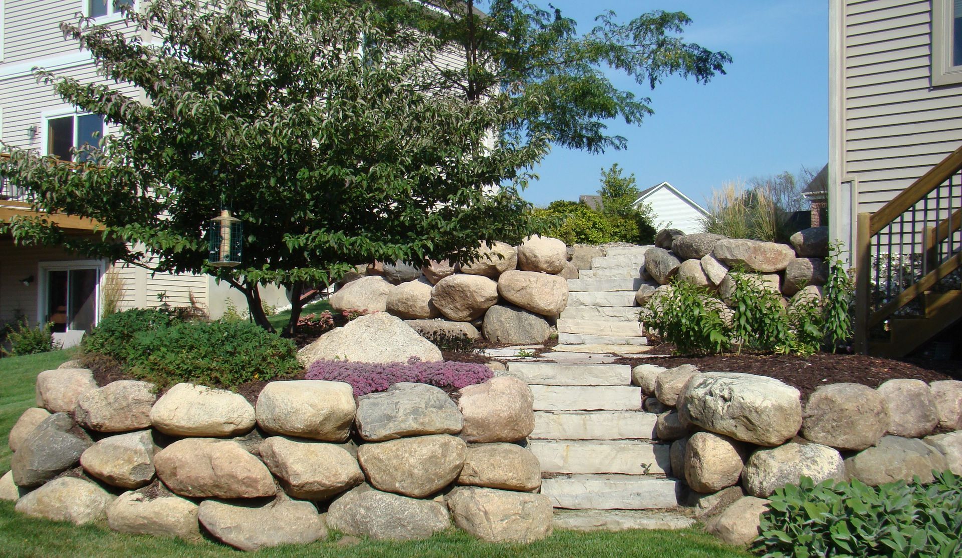 Stone retaining wall with steps leading up to a backyard garden.