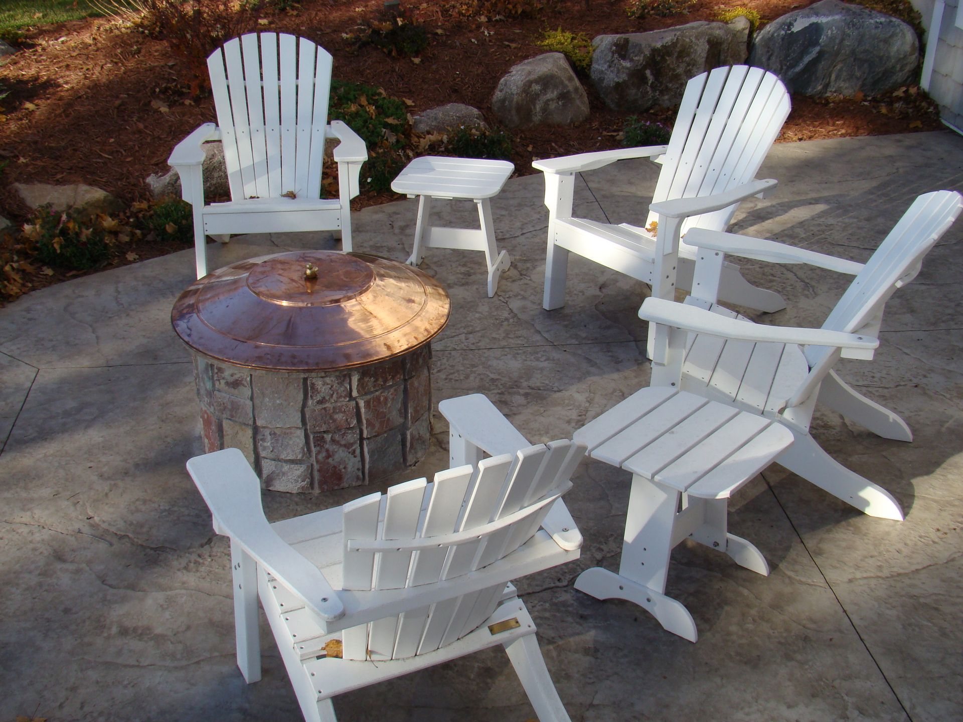 White Adirondack chairs around a fire pit on a patio.