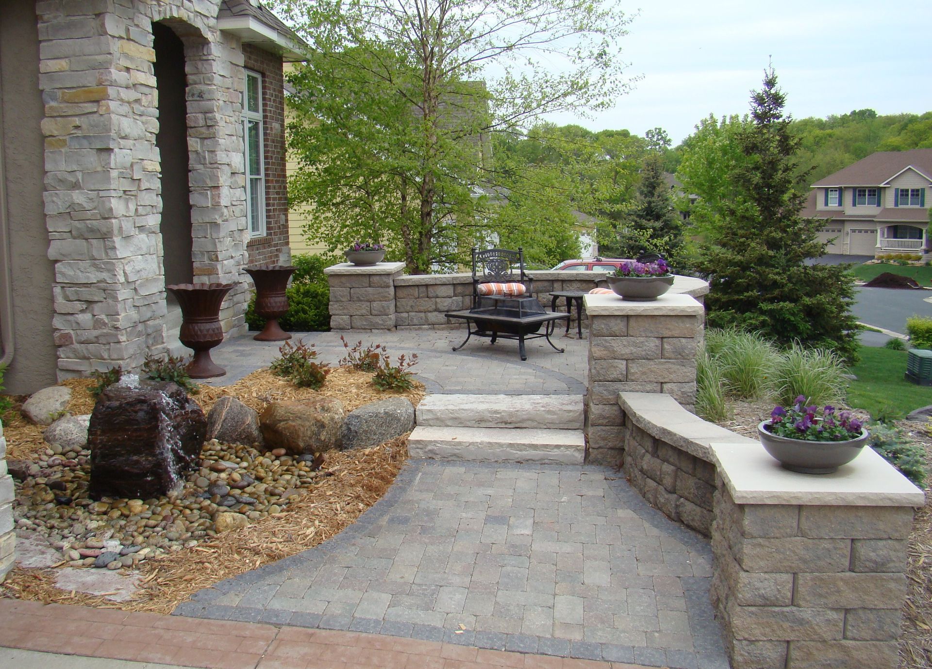 Stone patio with water feature, steps, and built-in seating with potted flowers.