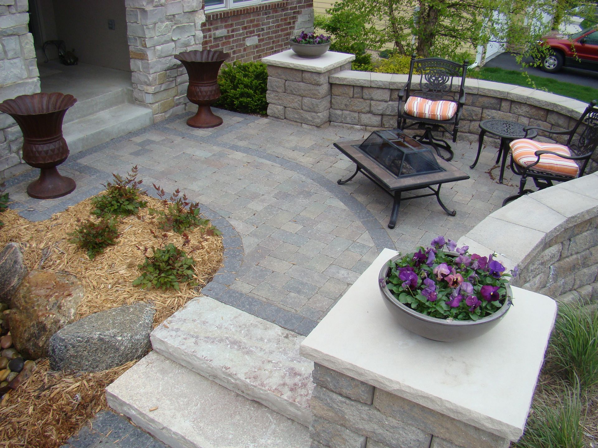 Stone patio with fire pit, seating, and potted flowers.