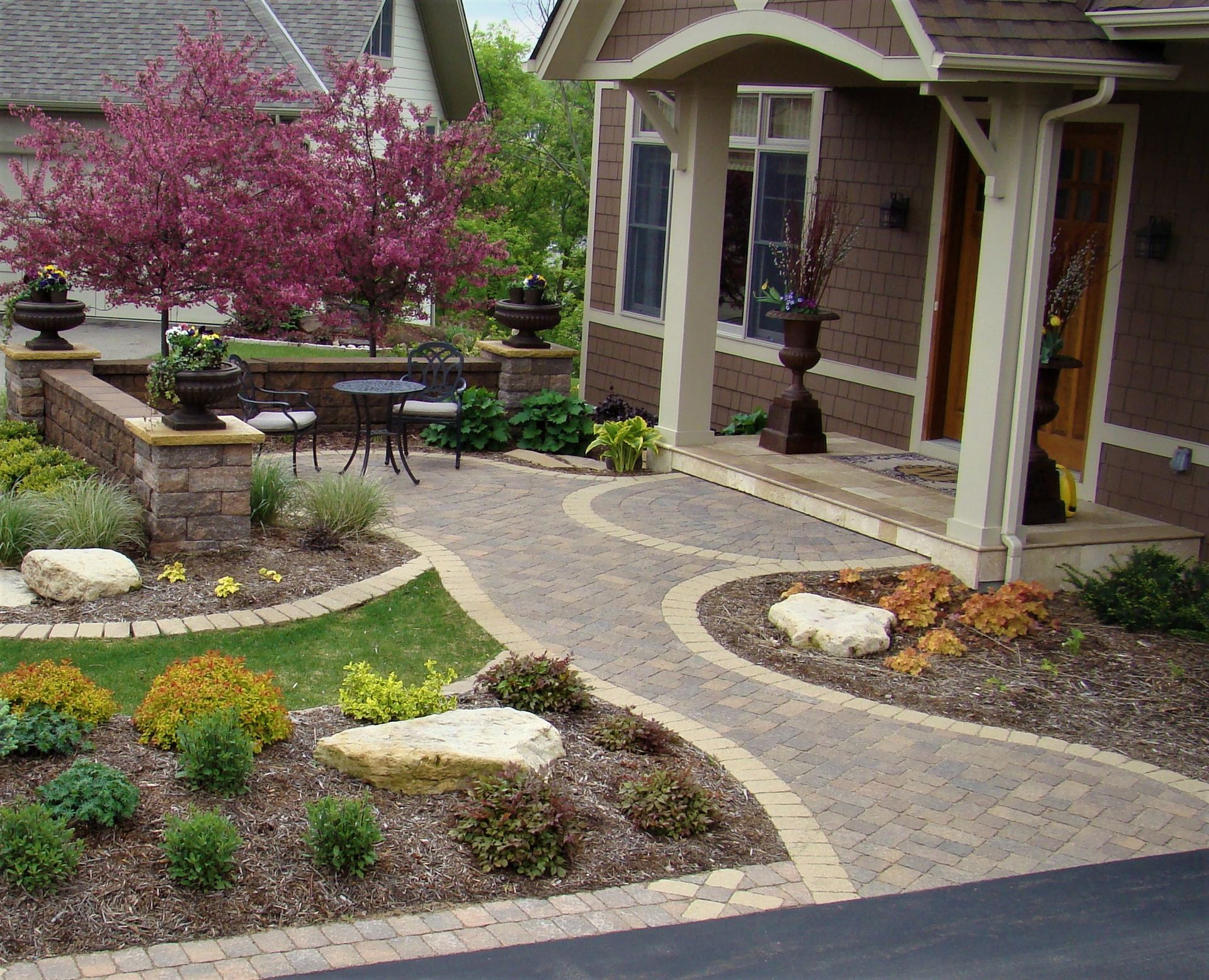 Stone pathway leading to a brown house with manicured landscaping and a small seating area.