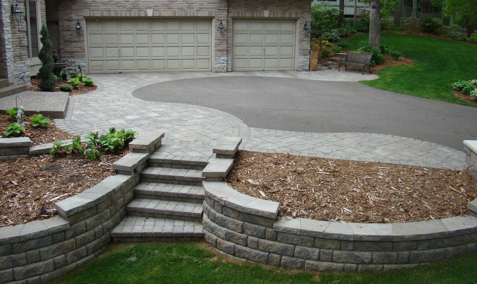 Driveway with curved brick steps and retaining walls, leading to a garage. Asphalt driveway.