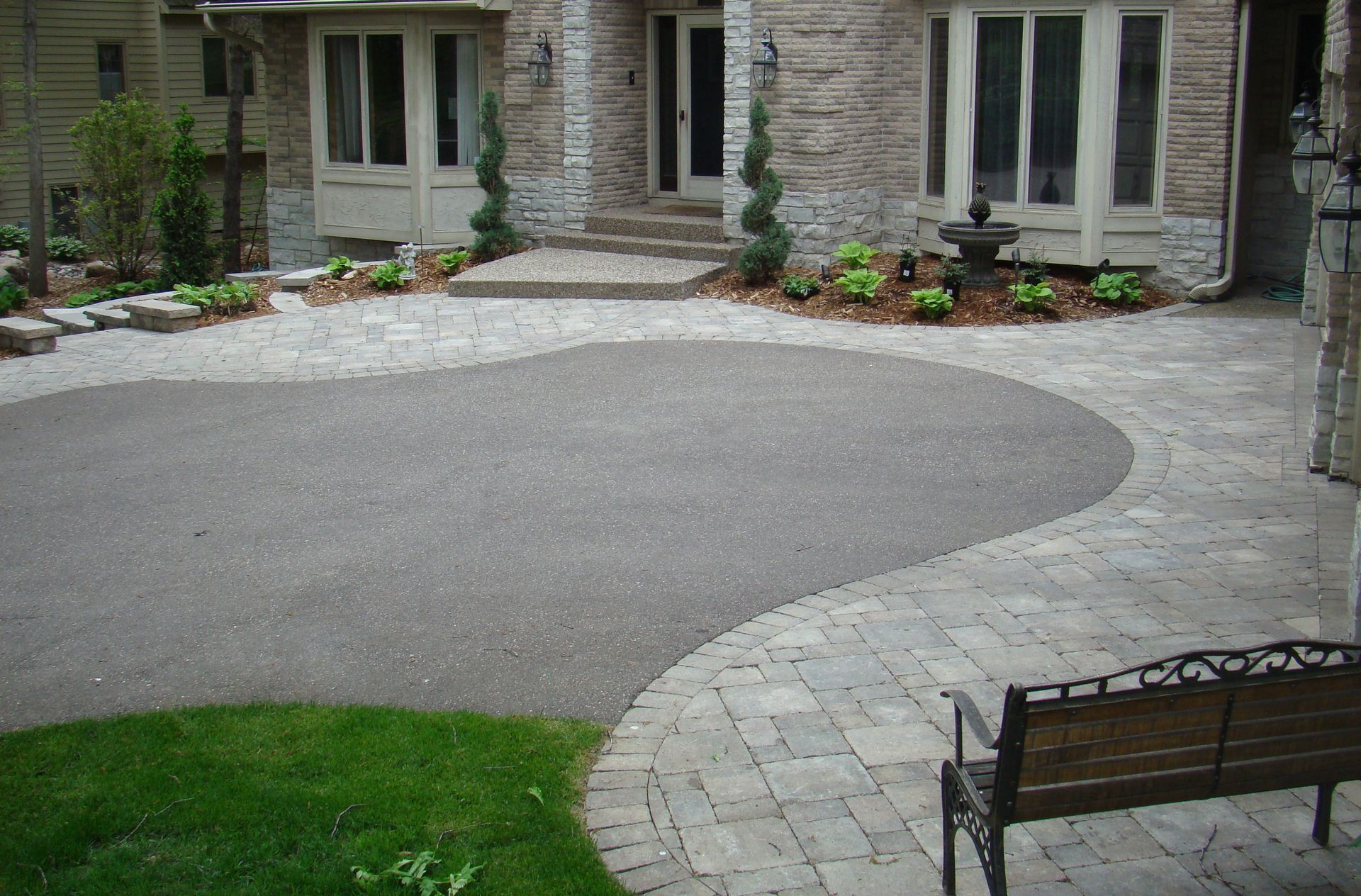 Front yard with stone facade, gravel drive, paved path, bench, and landscaping.