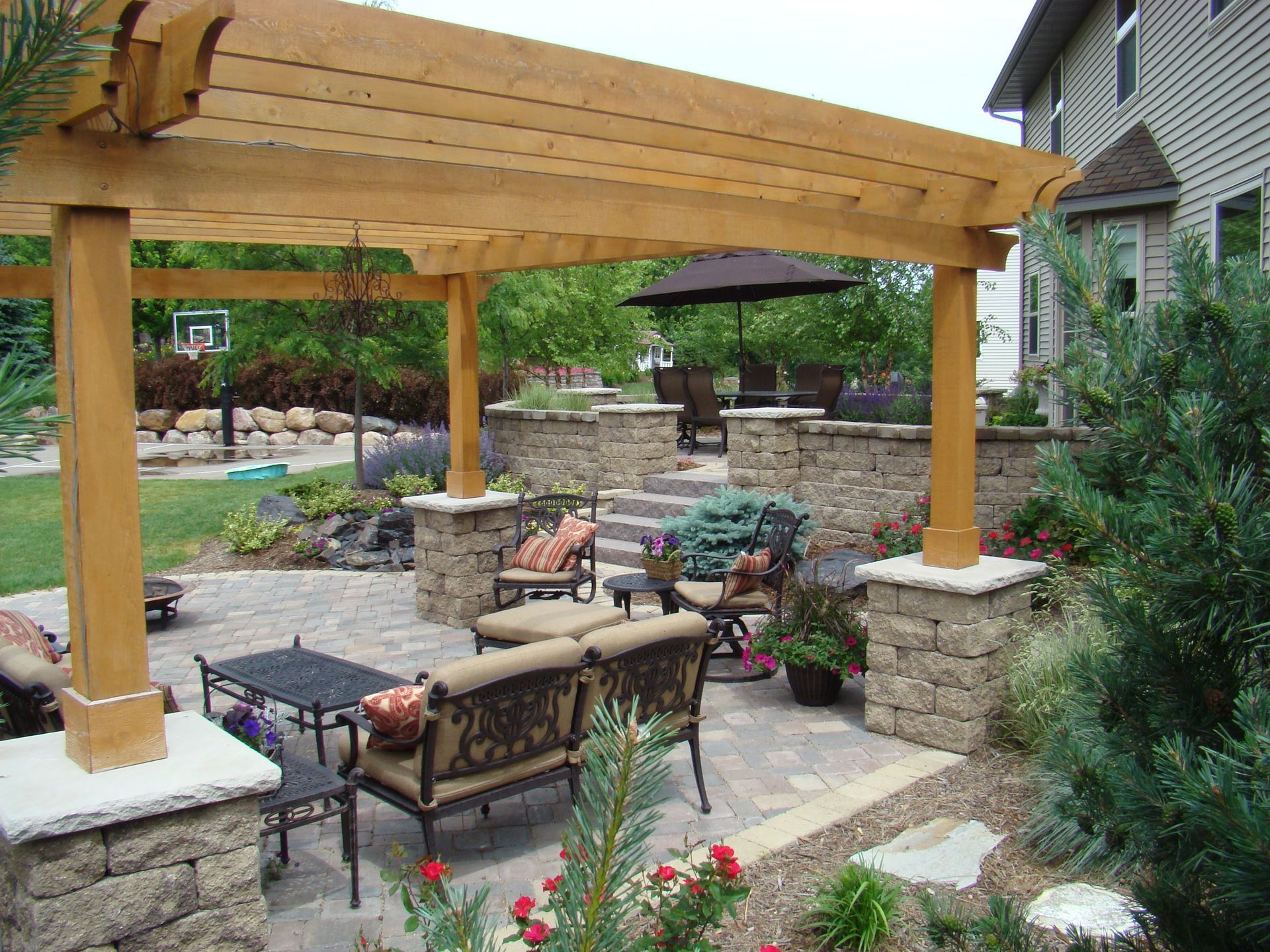 Patio with stone pavers, pergola, and outdoor furniture in a backyard setting with landscaping.