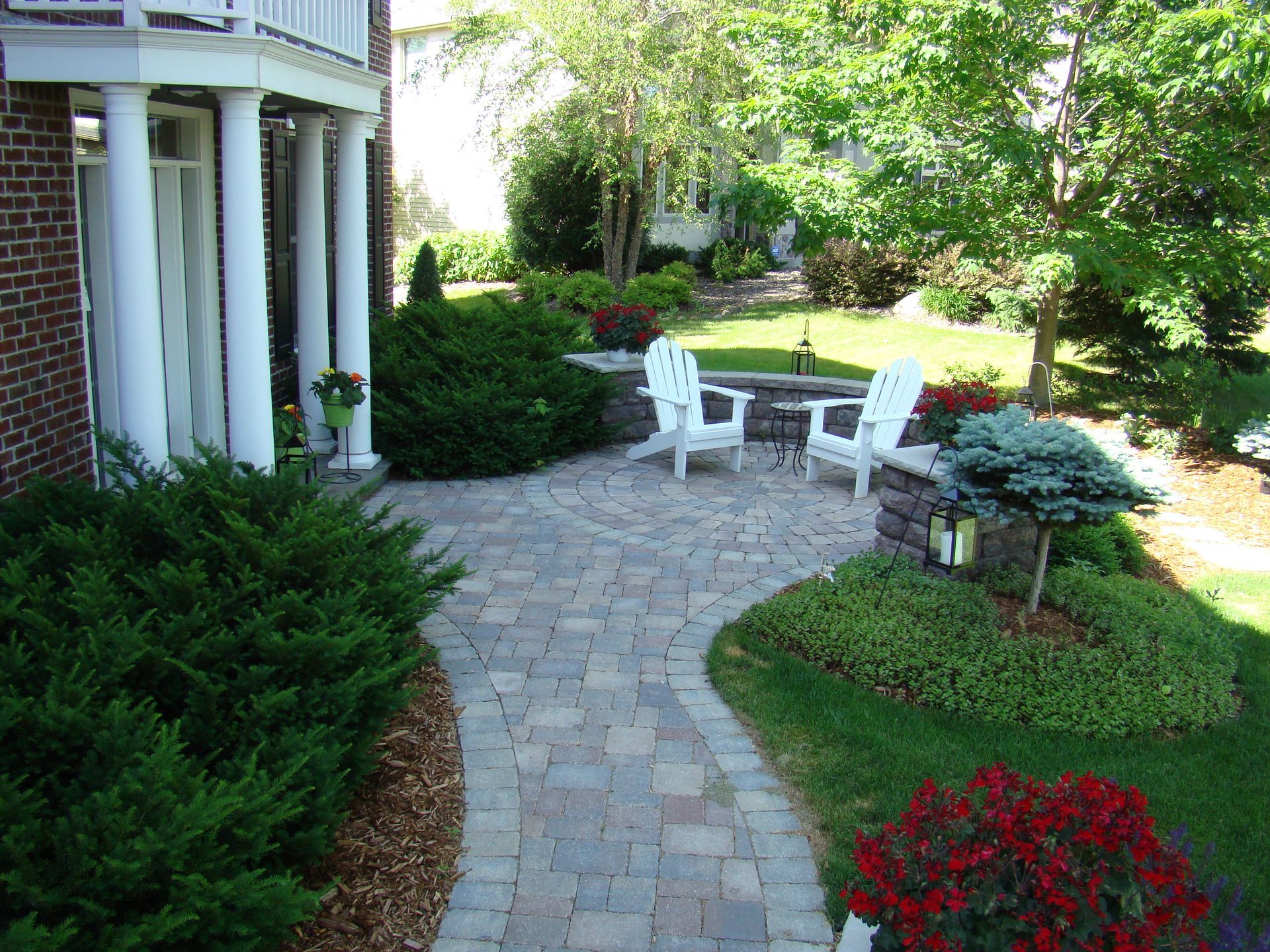 Brick home exterior with a stone patio, chairs, and garden landscaping.