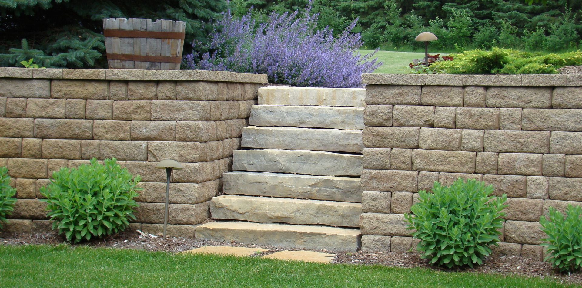 Stone steps and retaining walls in a landscaped garden with shrubs and purple flowers.
