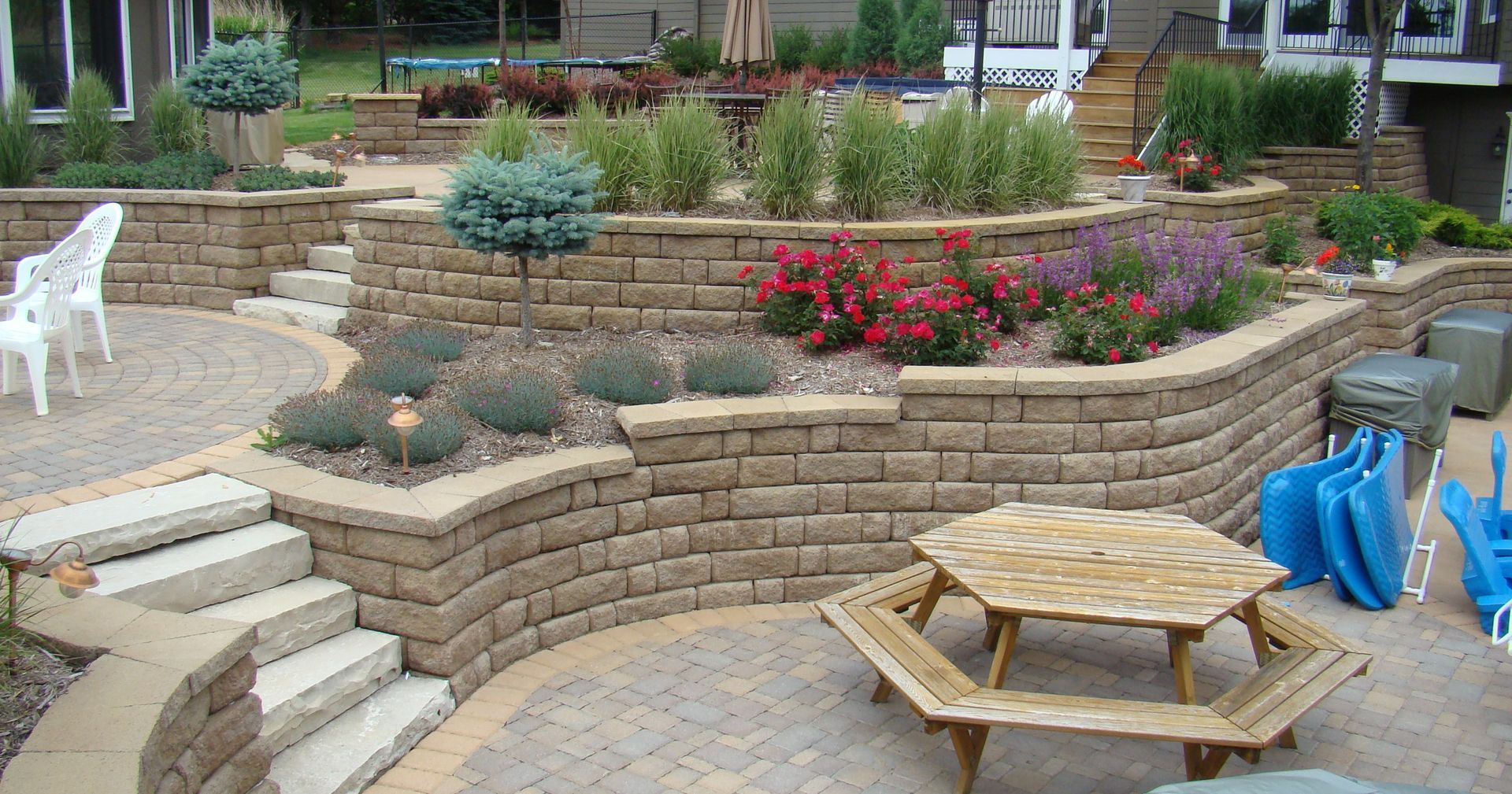Multi-tiered landscaped backyard with stone retaining walls, patio, and picnic table.