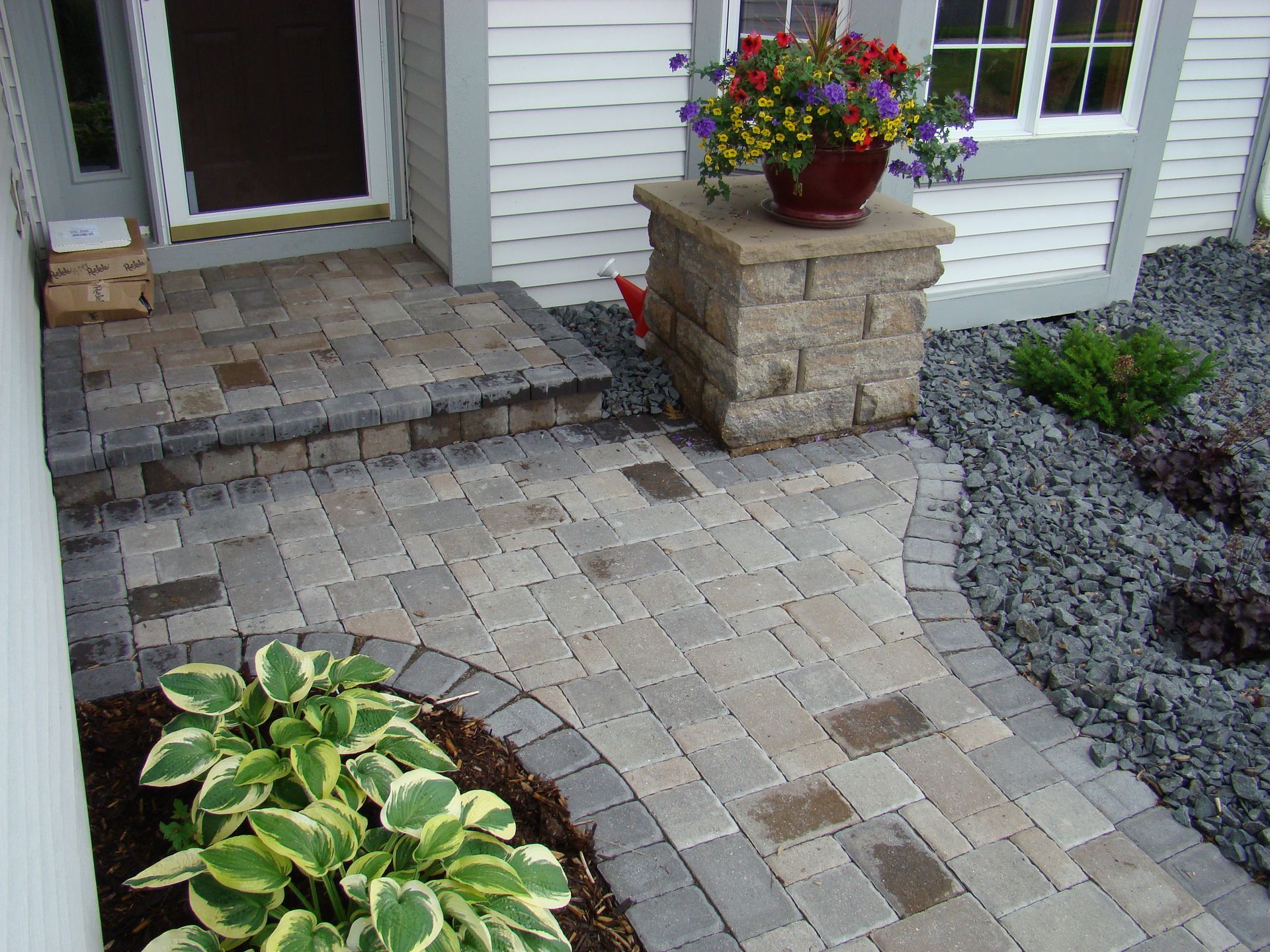 Brick walkway and steps leading to a front door with flower pots and landscaping.