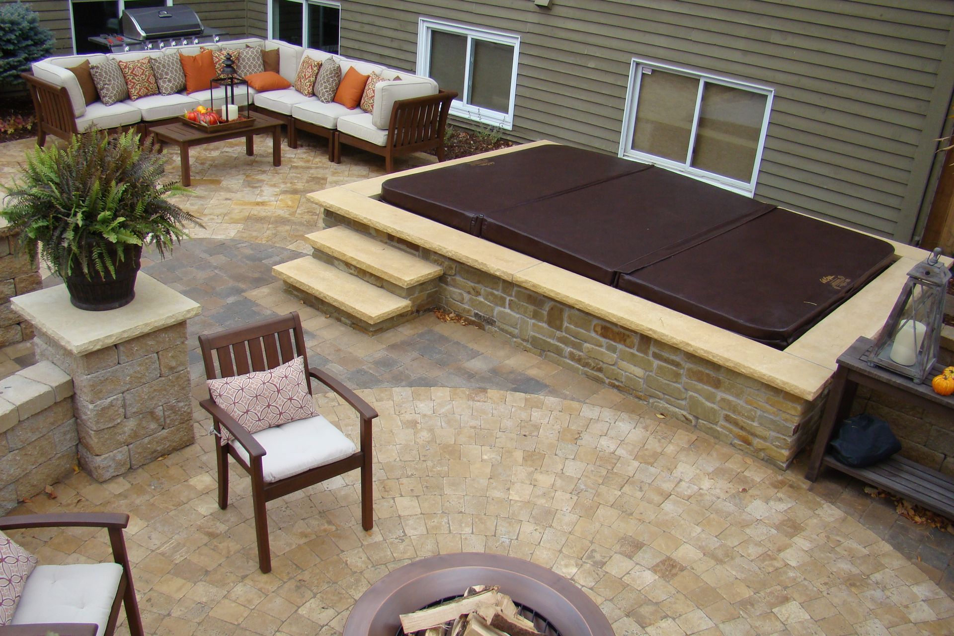 Patio with hot tub, seating, and fire pit. Brown and beige tones dominate.