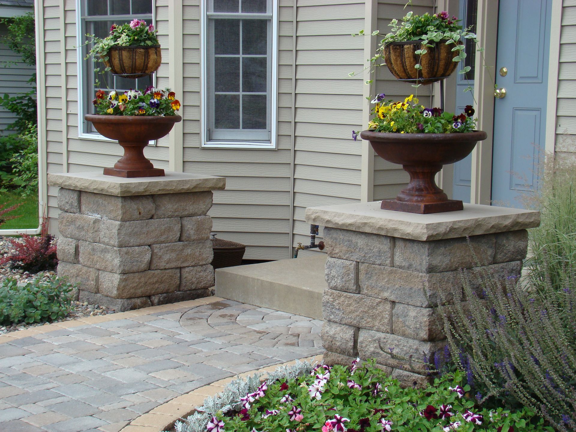 Two stone pillars with planters, a walkway, and a house facade.