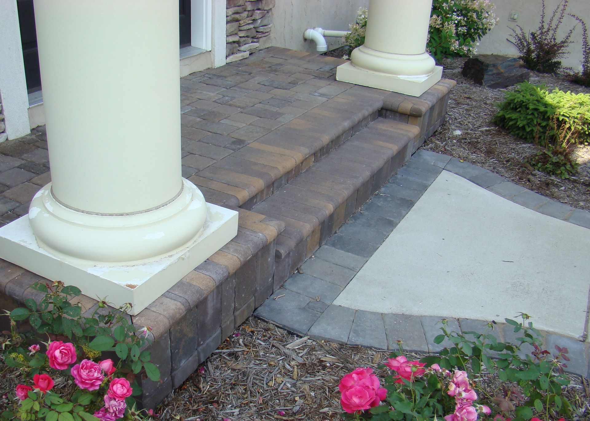Exterior entrance with beige columns, brick steps, and rose bushes.