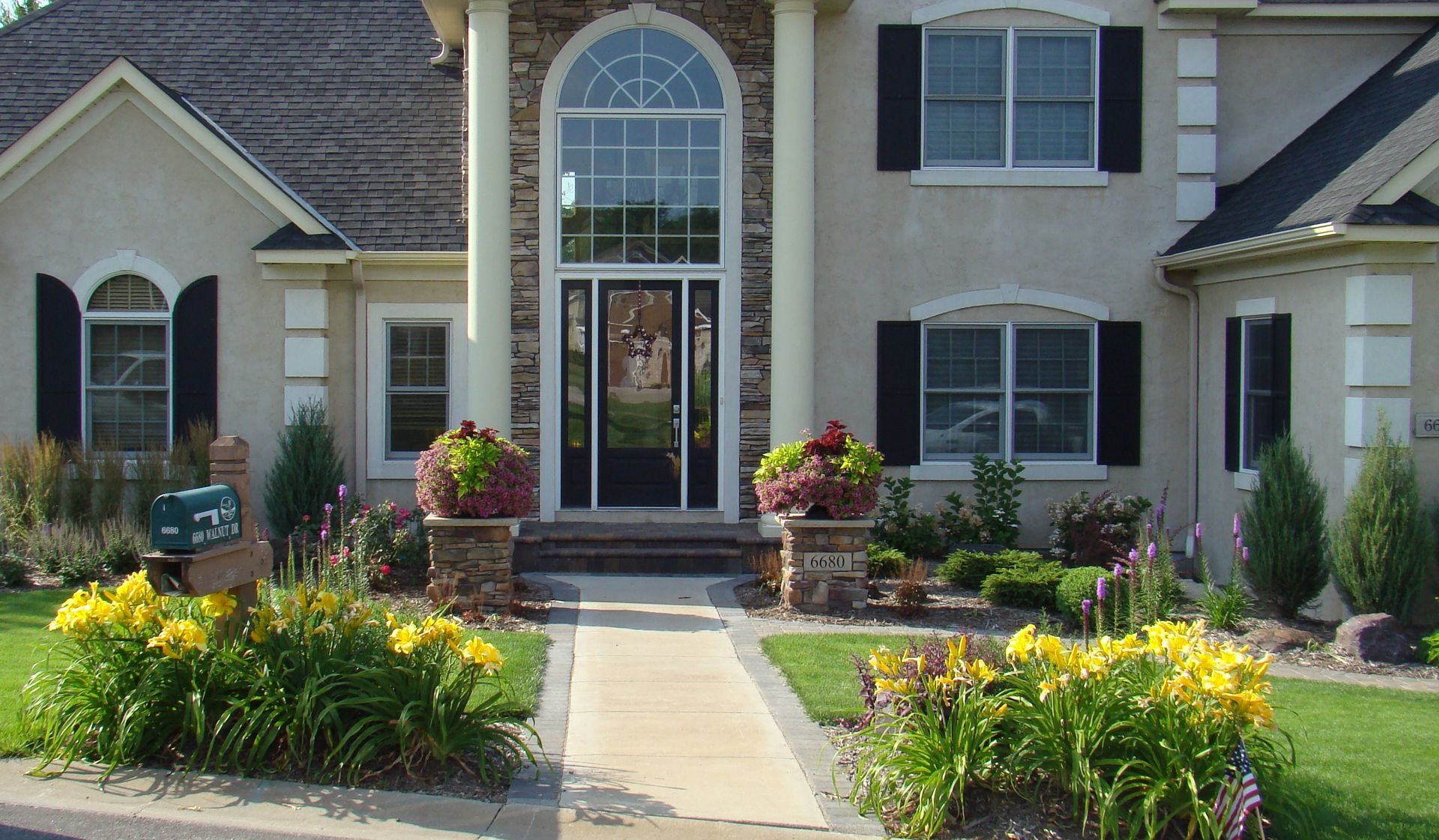 Beige house with a black front door, columns, and a landscaped walkway lined with flowers.