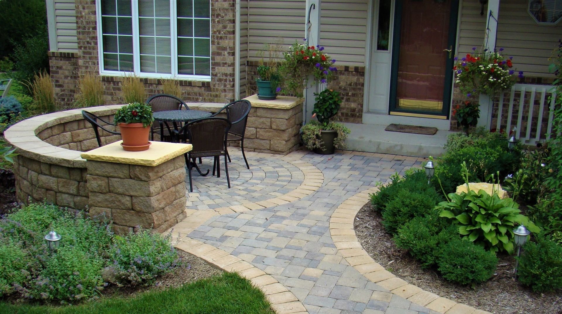 Brick patio with circular design, table and chairs, and surrounding greenery.