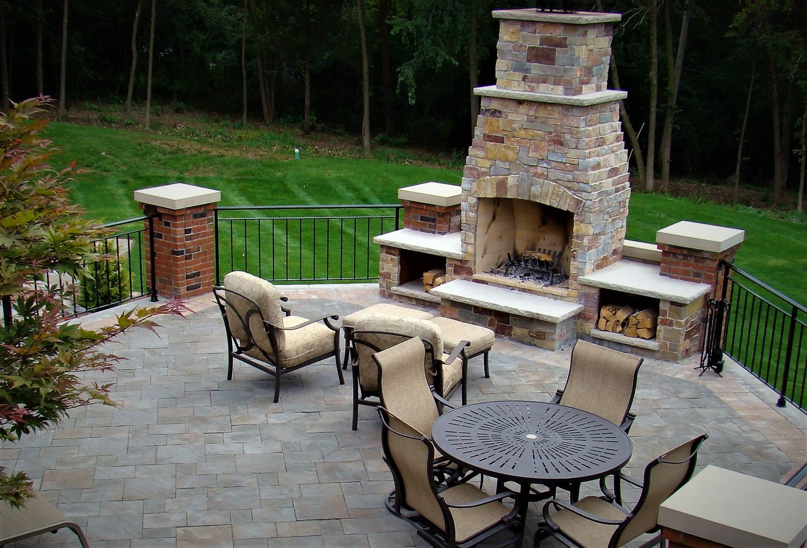 Outdoor patio with fireplace, seating, and green lawn. Fireplace has stone facade.