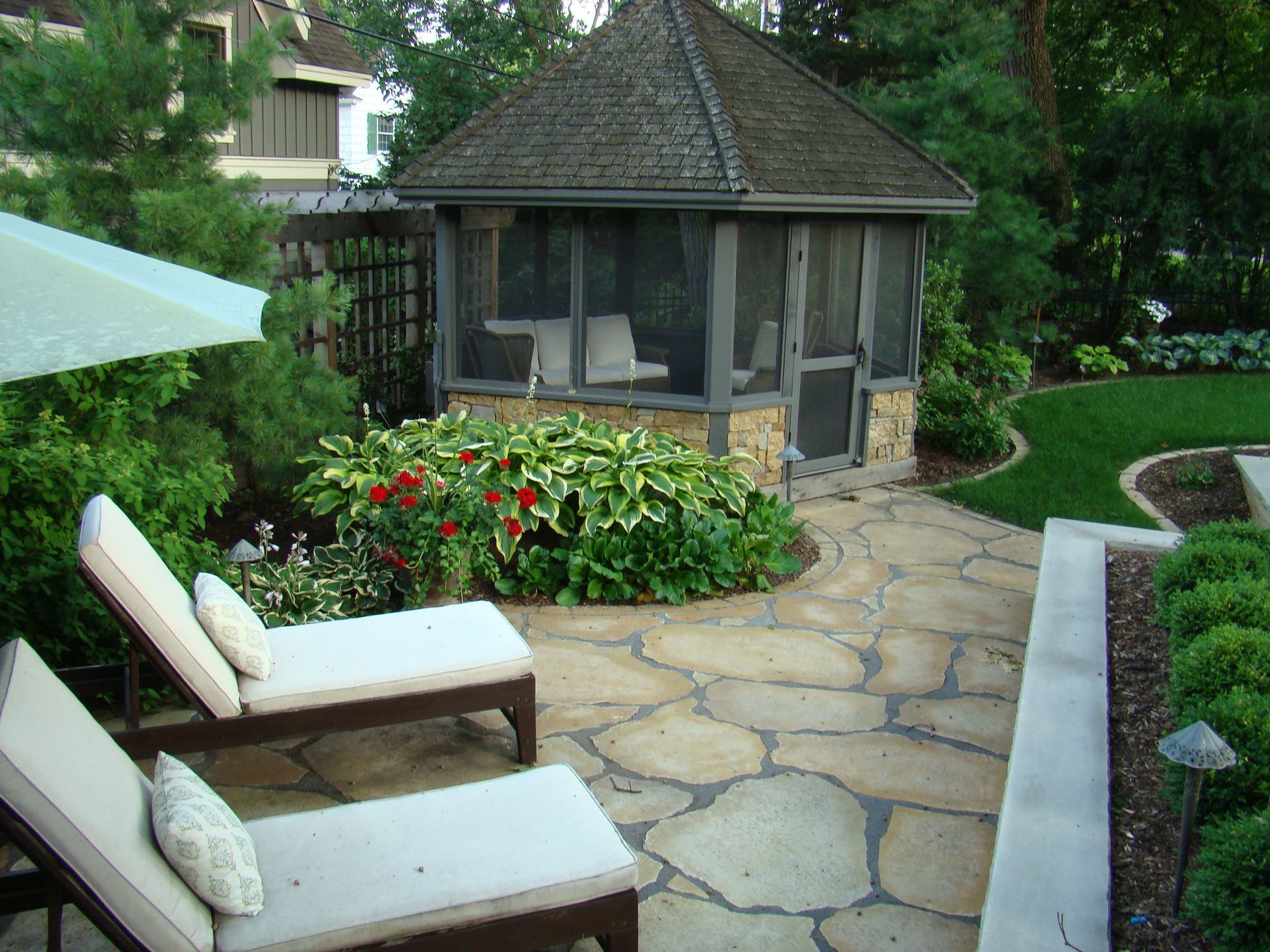 Stone patio with lounge chairs, screened gazebo, and lush landscaping.