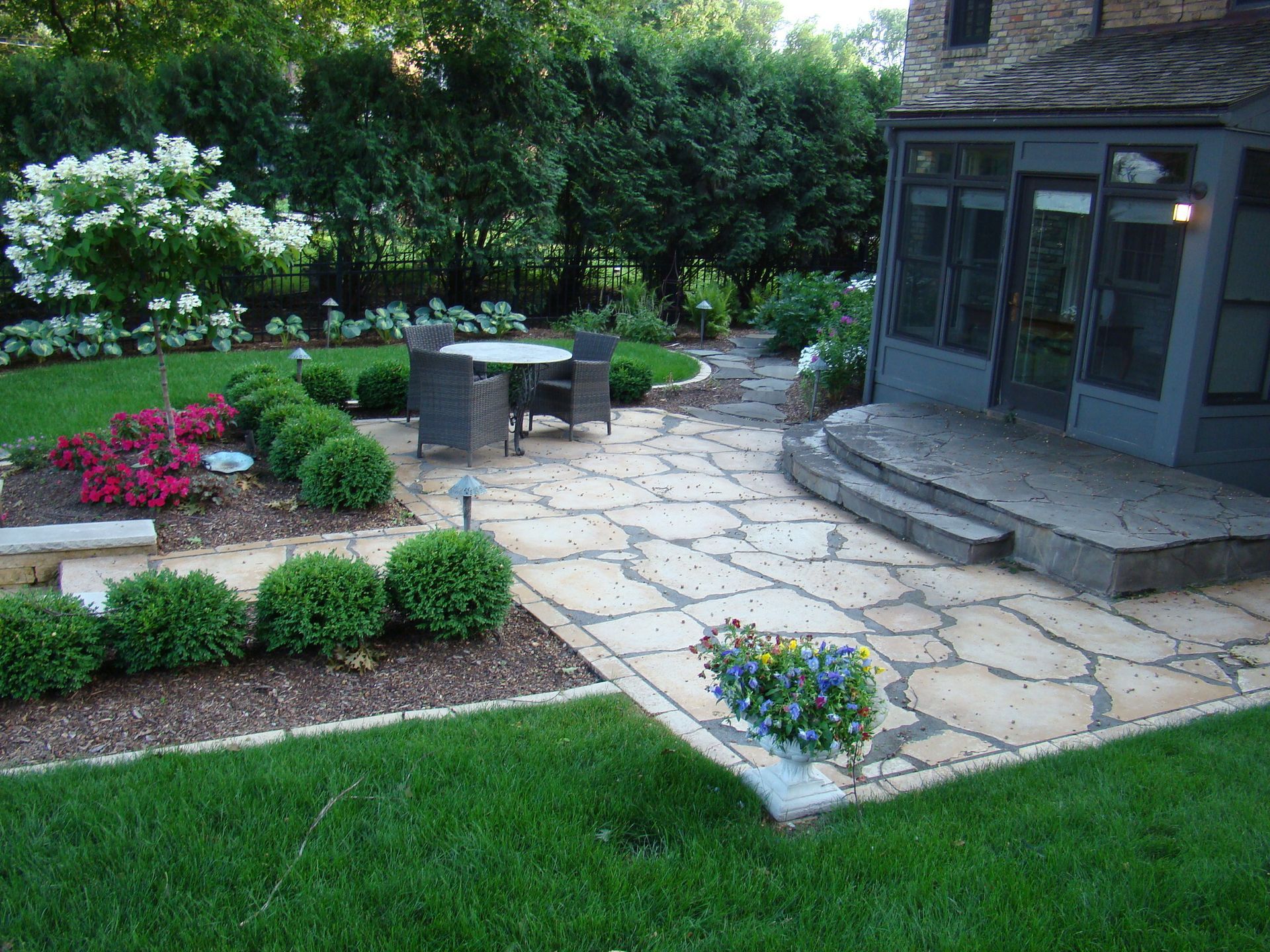 Stone patio with outdoor furniture, landscaped garden, and house in the background.