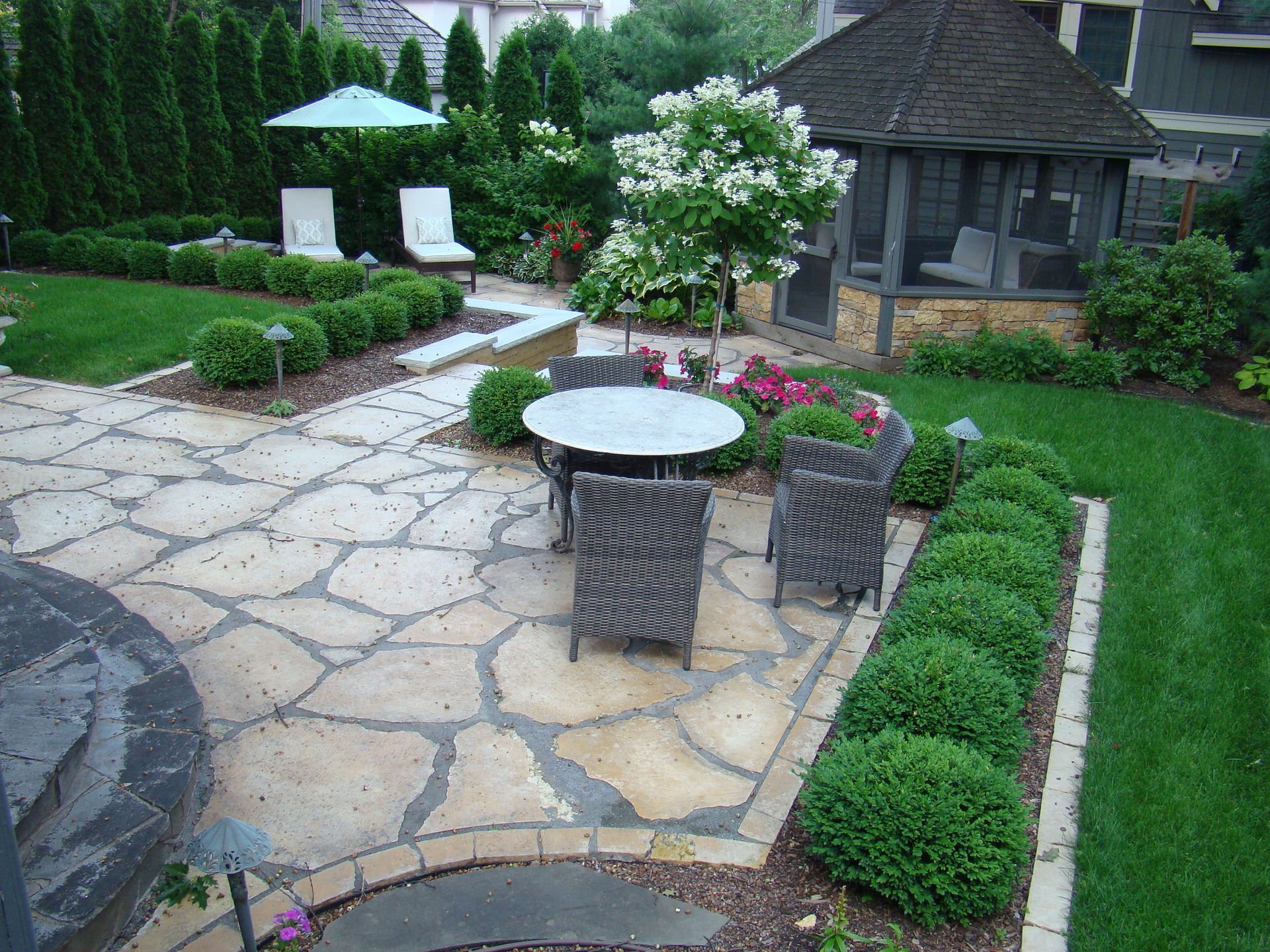 Stone patio with outdoor furniture, landscaping, and a gazebo in a backyard.