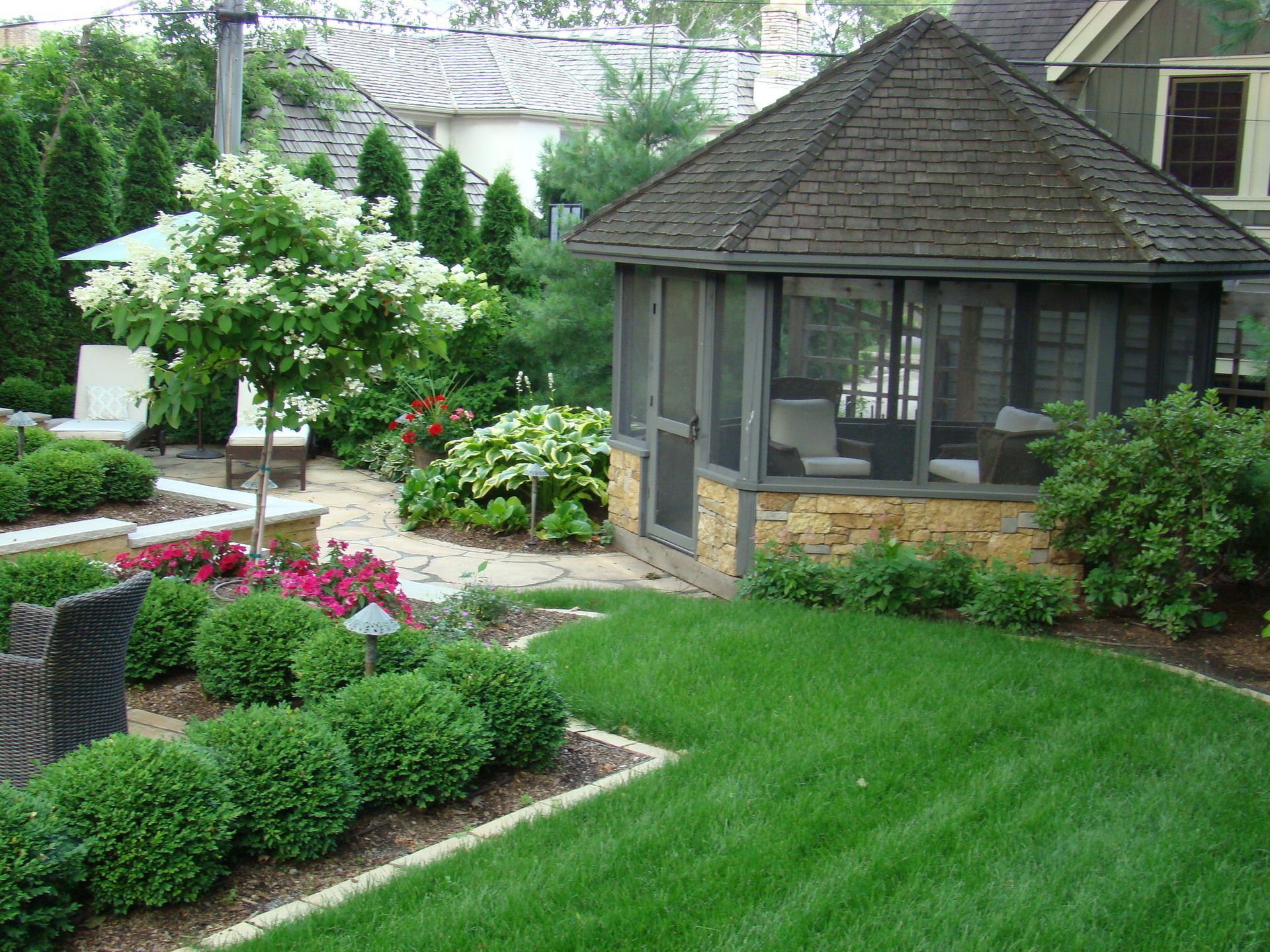 Lush backyard with gazebo and manicured landscaping, featuring green grass, shrubs, and flowering plants.