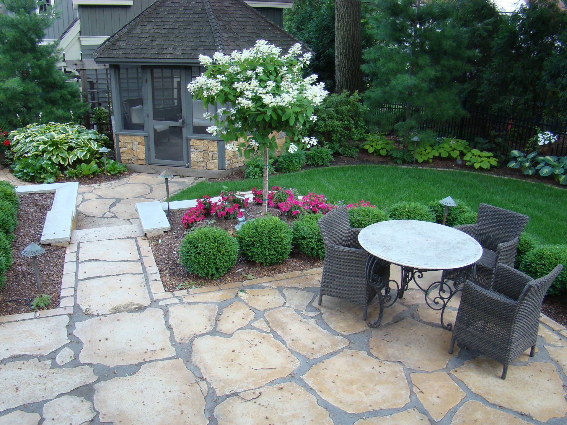 Stone patio with table and chairs, flower bed, and small gazebo.
