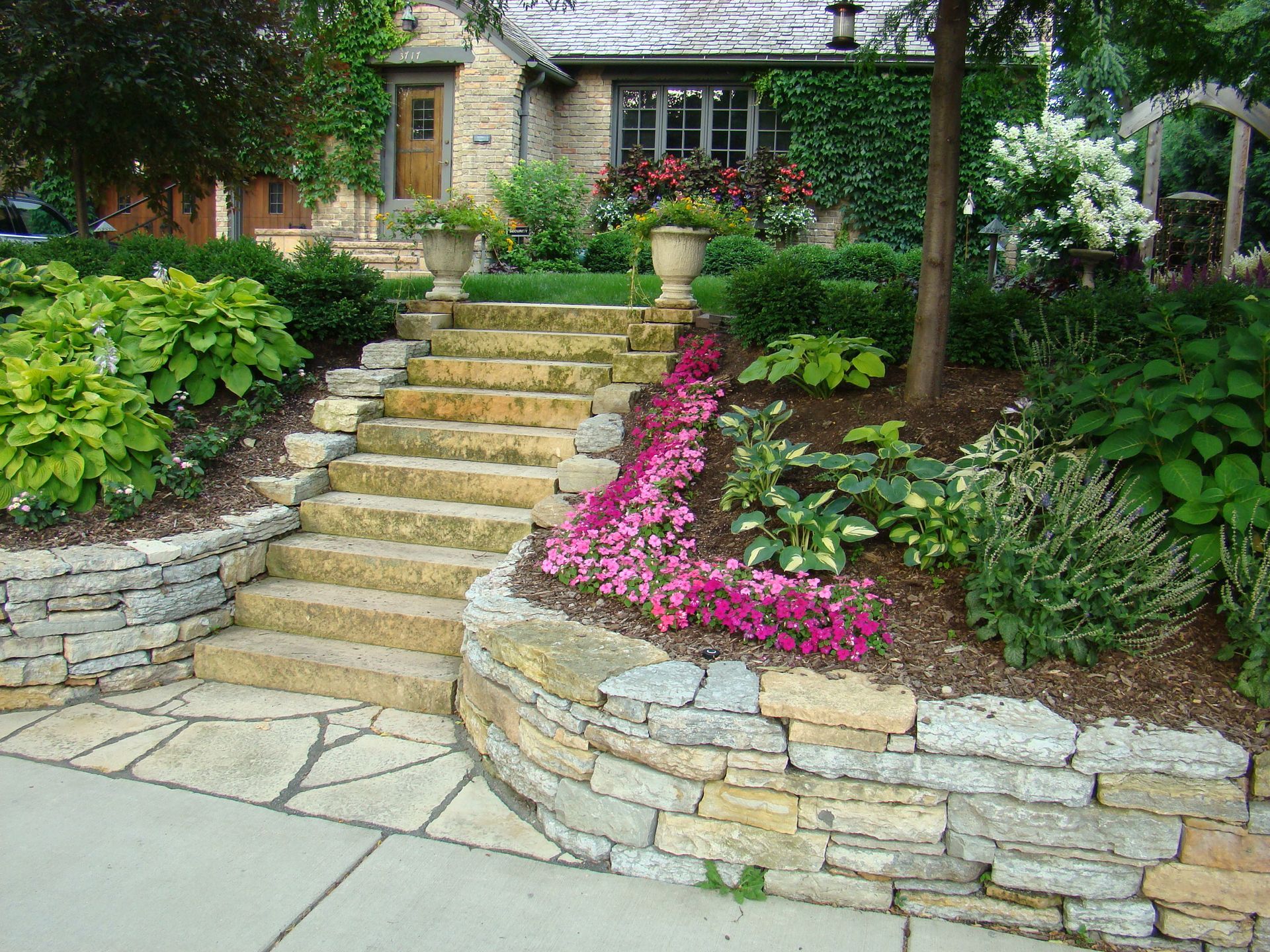 Stone steps leading up to a house with lush landscaping, including flowers and shrubs.