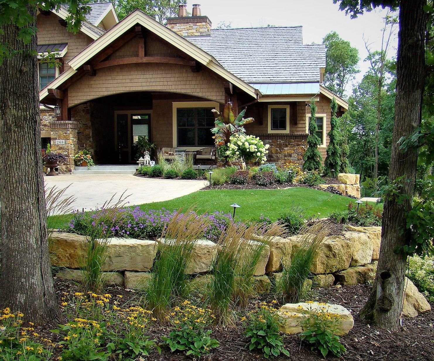 Cottage-style home with tan stucco, stone accents, and a landscaped front yard with a retaining wall.