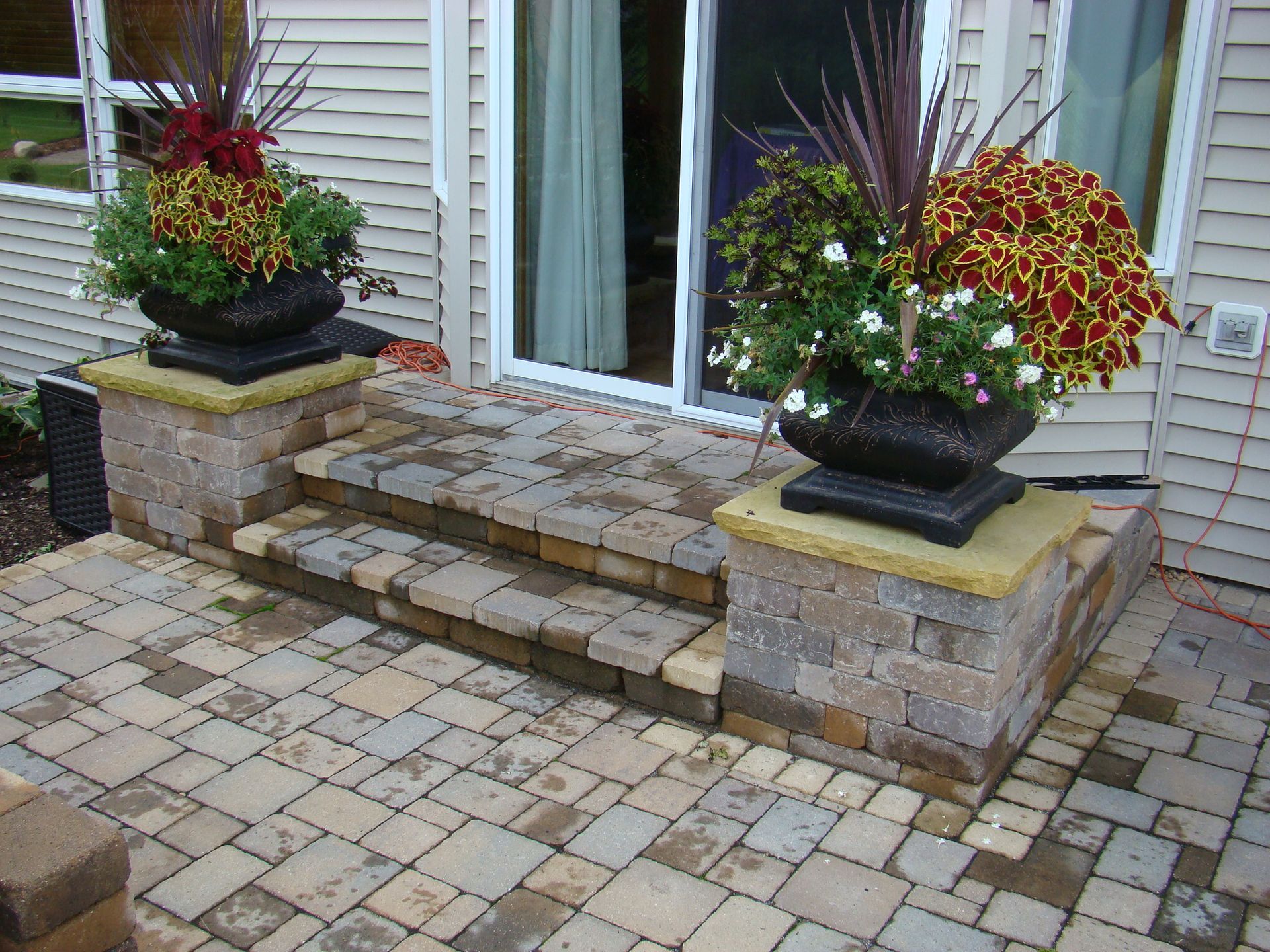 Brick patio with stone steps leading to sliding glass doors, topped with potted plants.