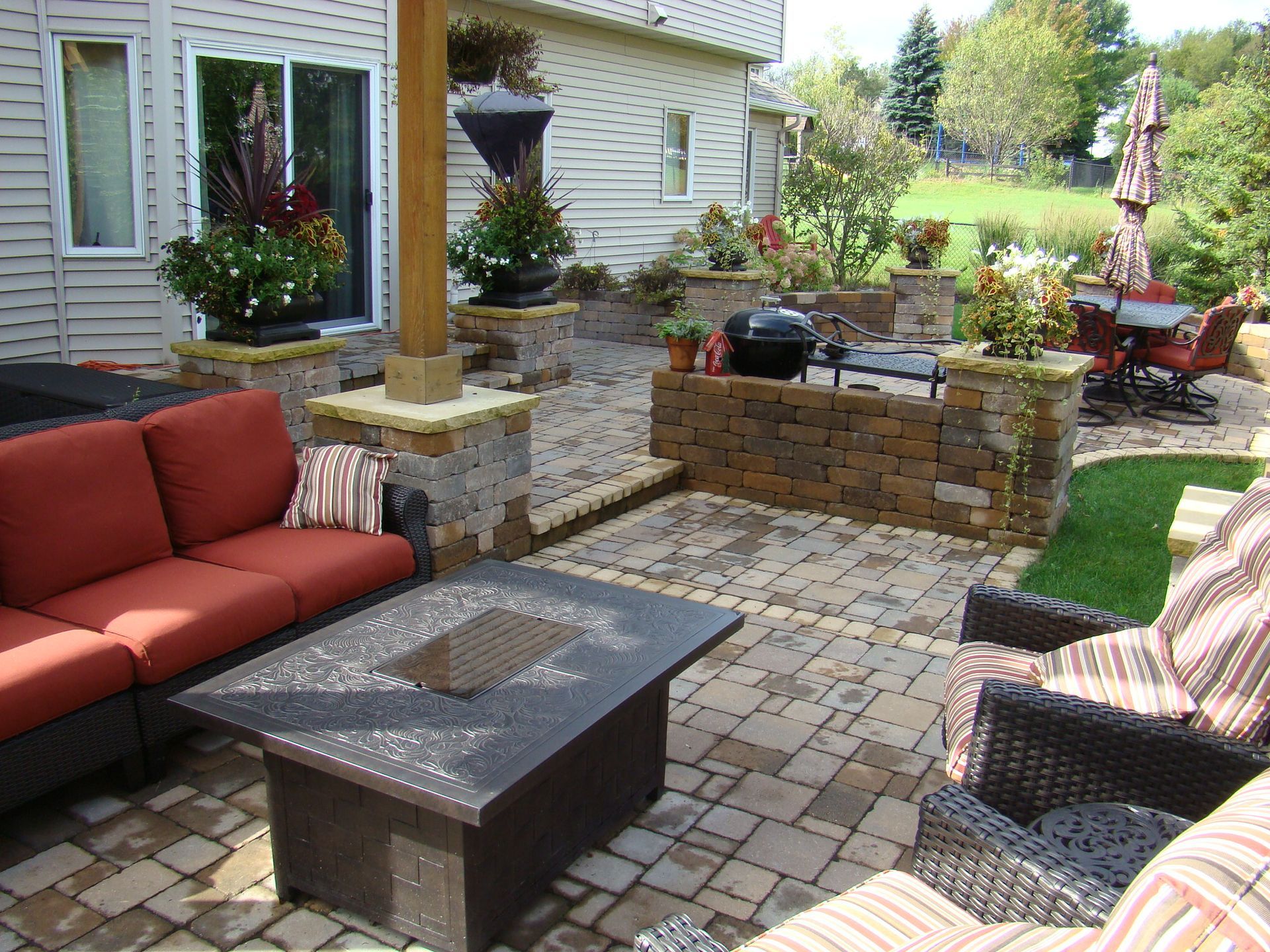 Backyard patio with fire pit, seating, grill, and decorative planters.