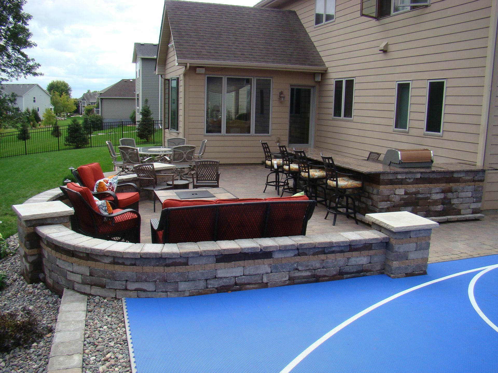 Backyard patio with built-in seating, fireplace, and outdoor kitchen. Basketball court in foreground.