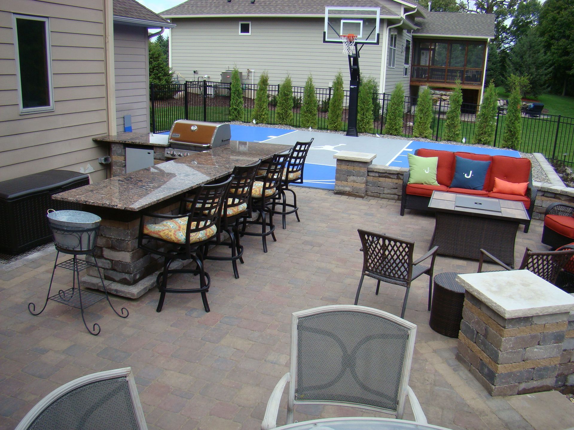 Backyard patio with bar, seating, and basketball court.