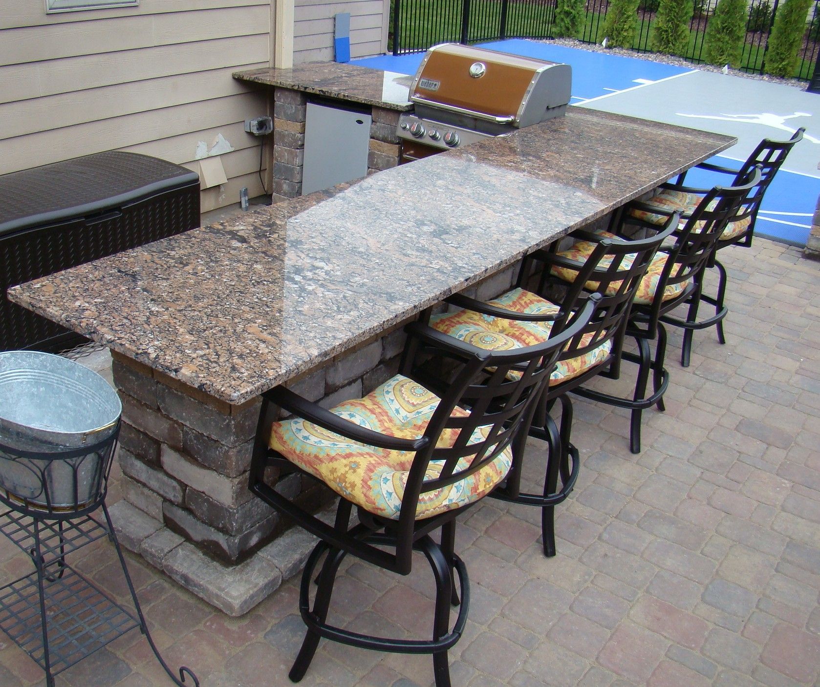 Outdoor kitchen with granite countertop, built-in grill, bar seating, and stone facade.