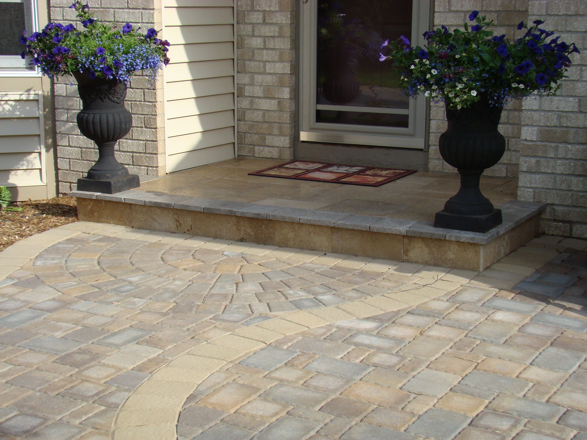 Stone patio and steps with urns of blue flowers flanking a doorway.