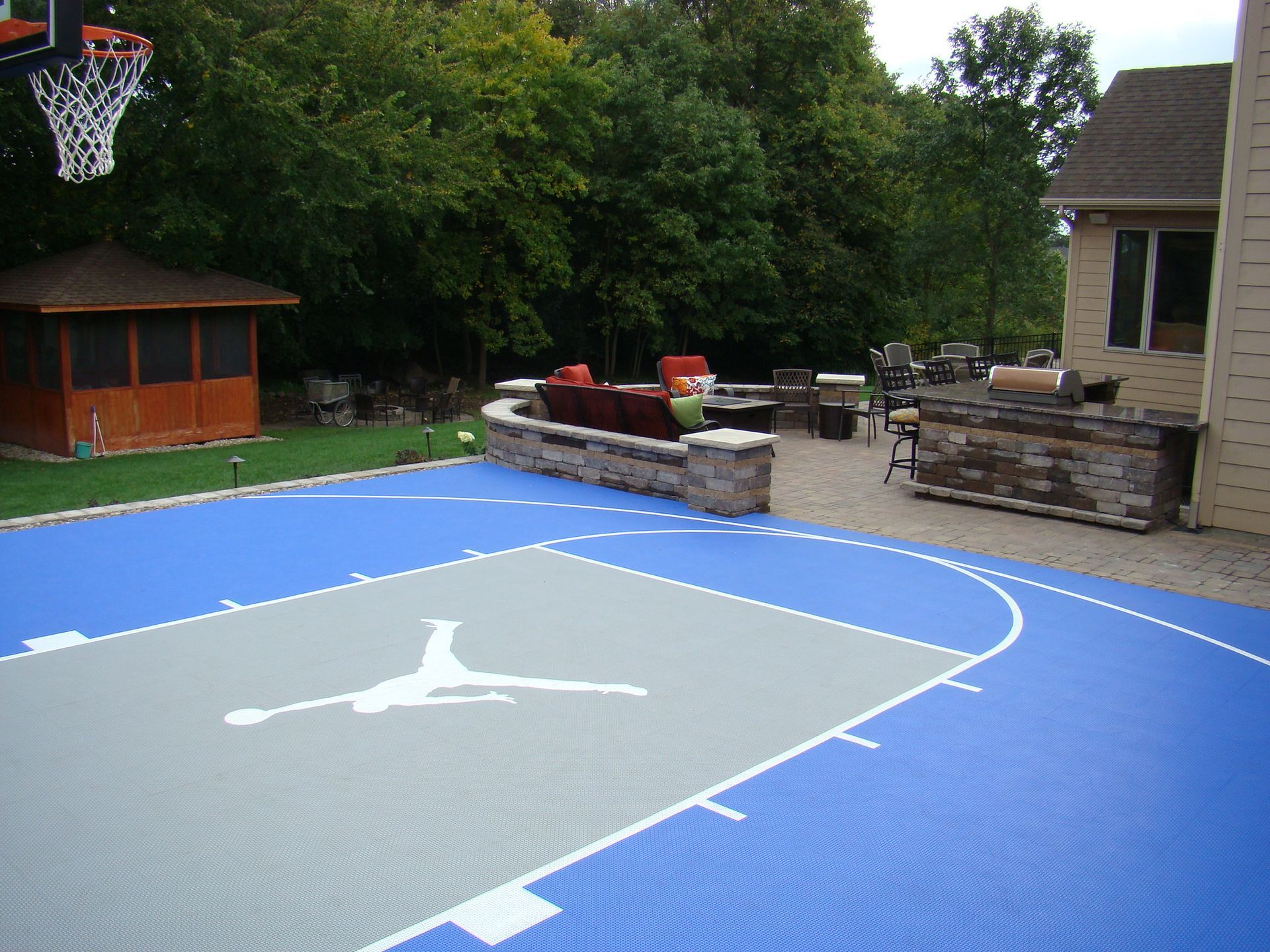 Outdoor basketball court with Michael Jordan logo, blue and grey tiles, gazebo, and patio.