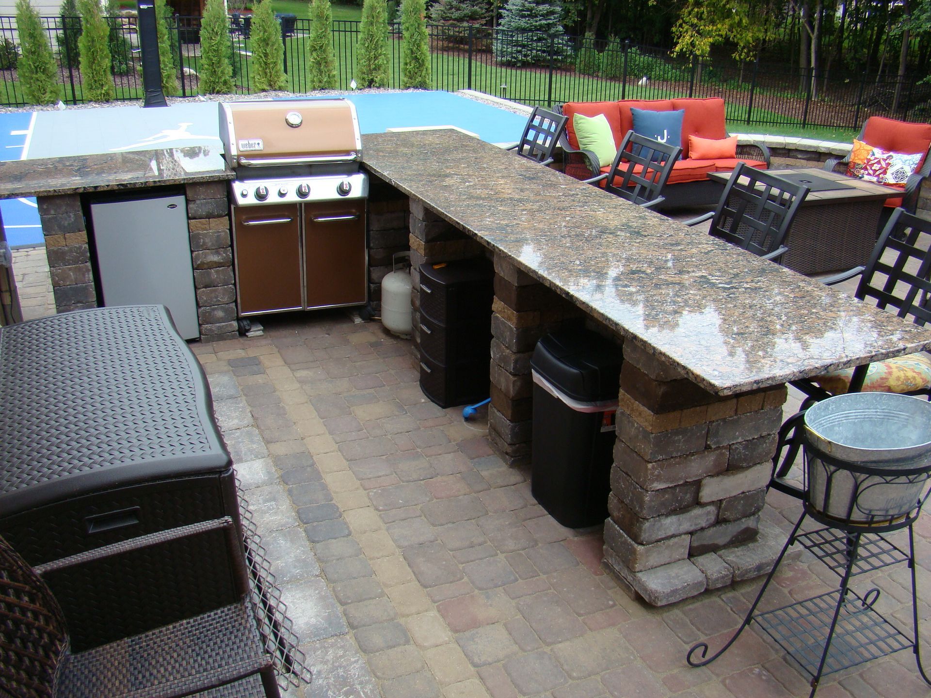 Outdoor kitchen with grill, countertop, seating, and basketball court.