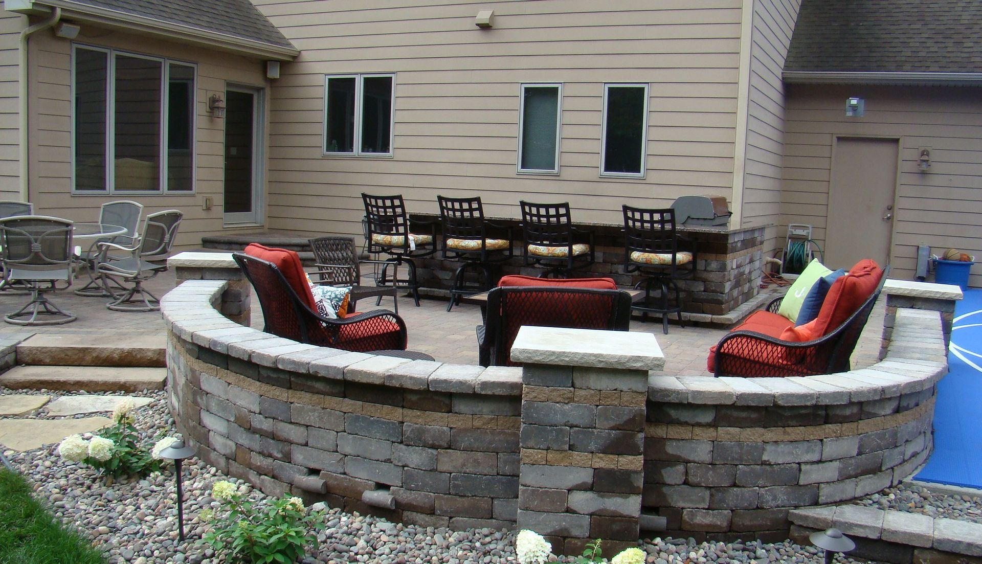 Brick patio with seating, fire pit, and bar area, with a house in the background.