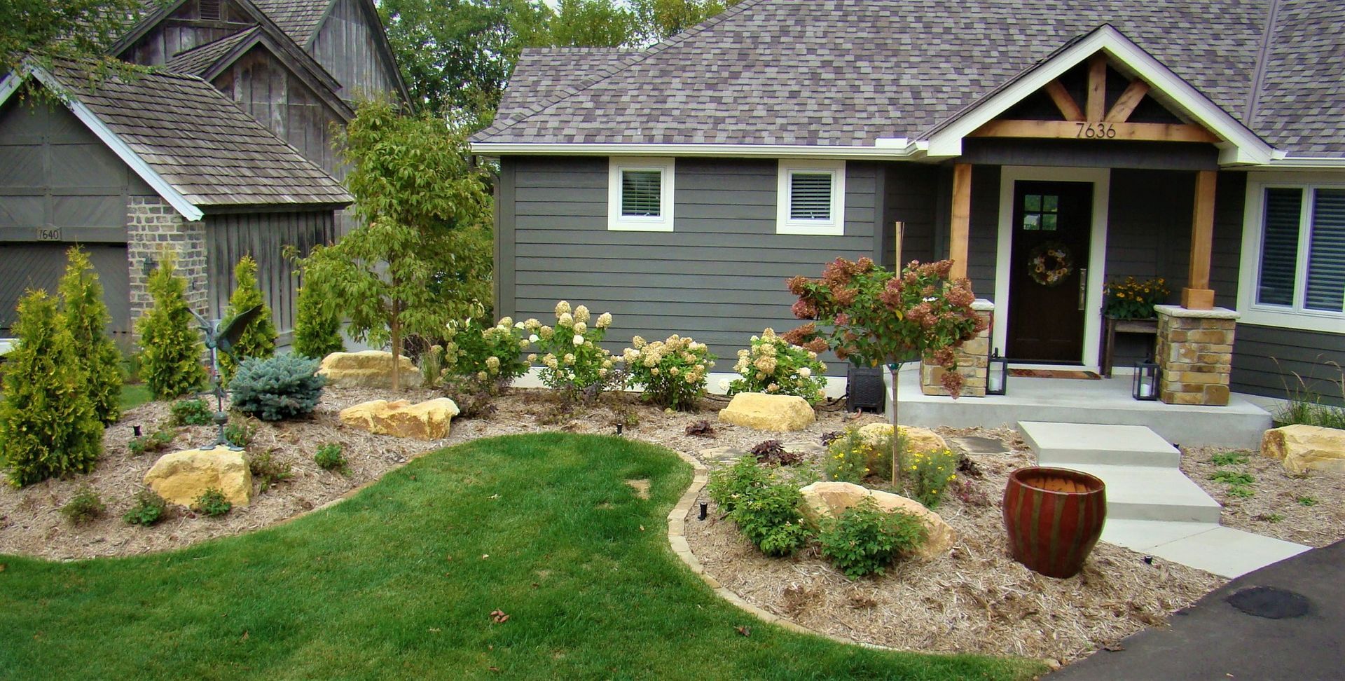 Landscaped front yard with a gray house and a wooden shed.