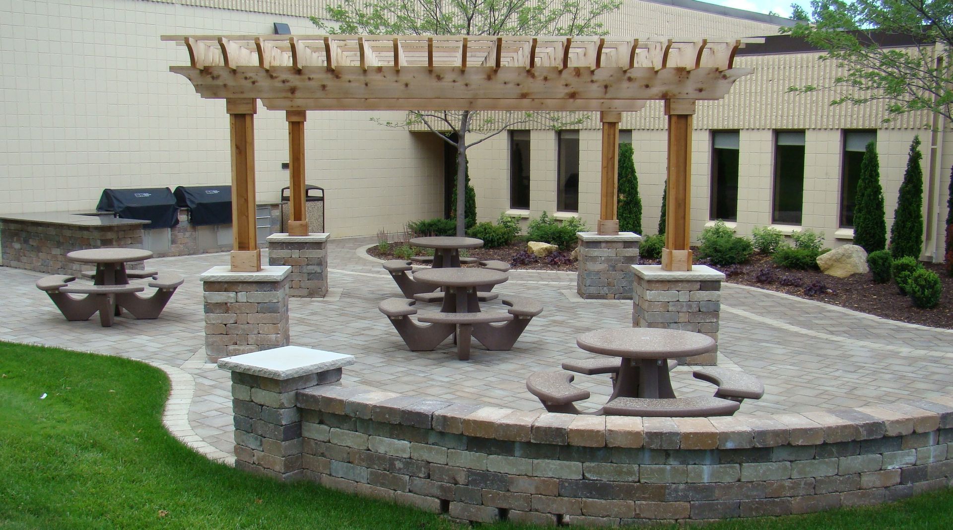 Outdoor patio with a pergola, tables, and a brick retaining wall.