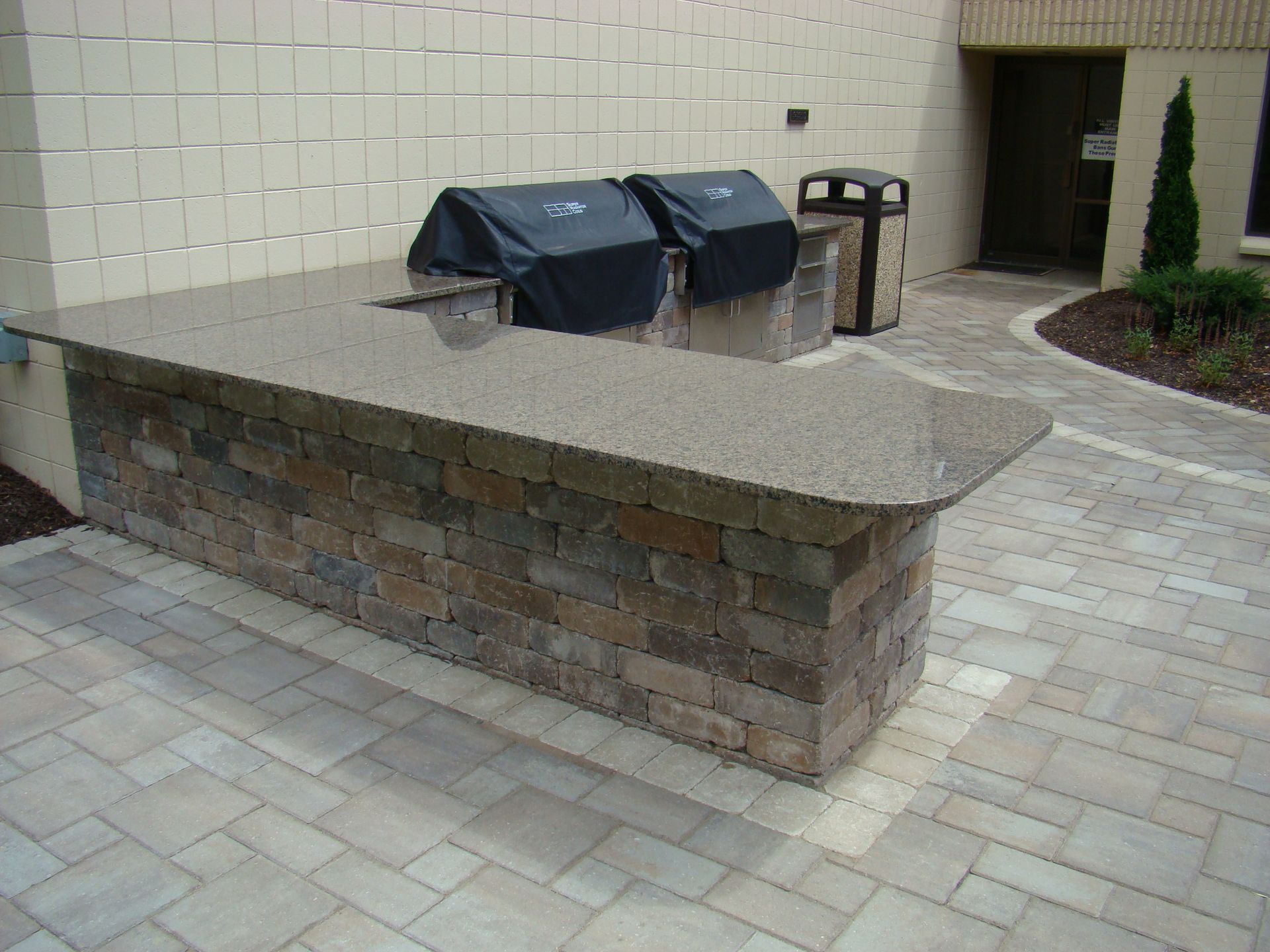Outdoor grilling station with brick facade and granite countertop. Two grills are covered.