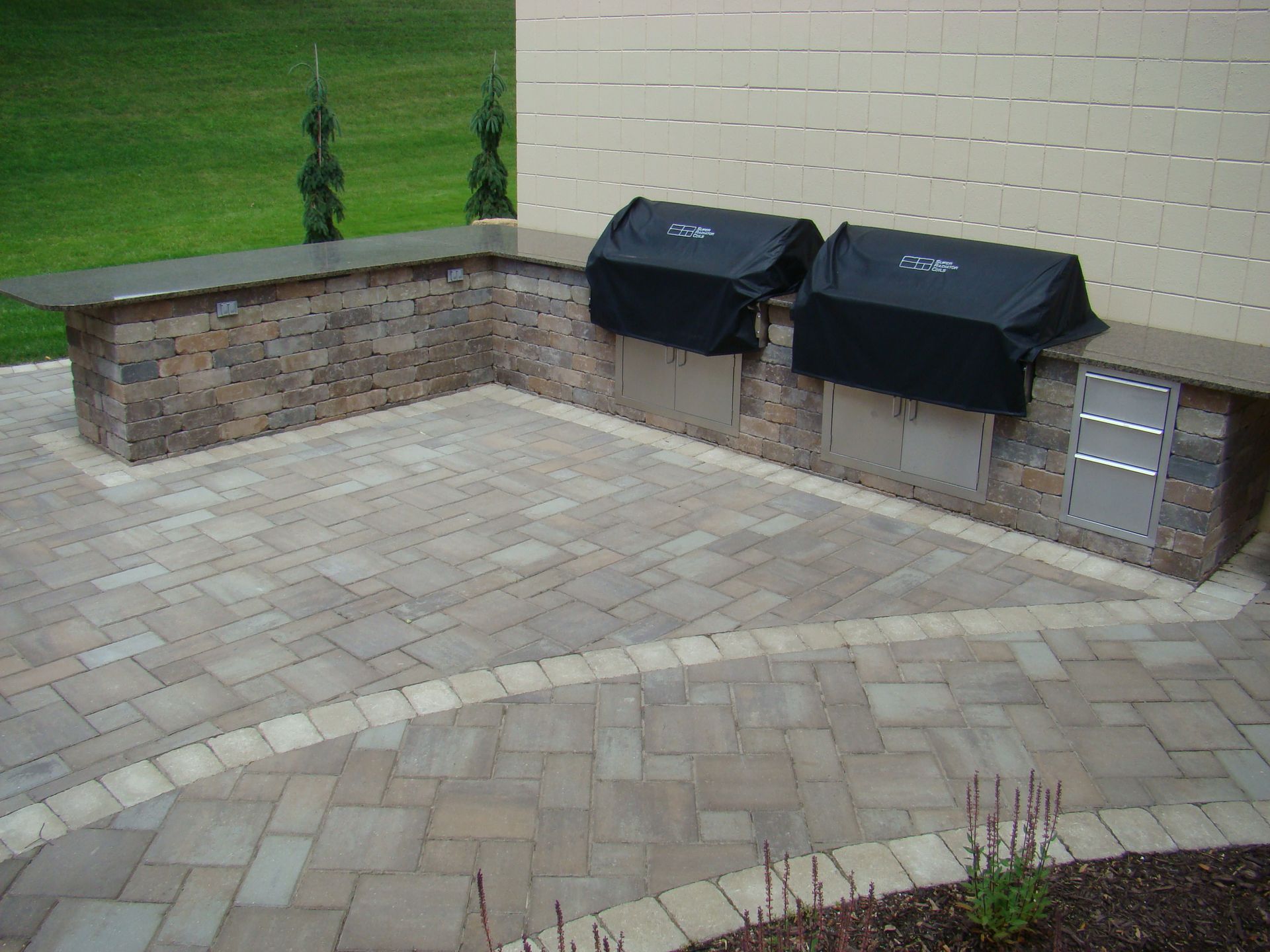 Outdoor kitchen with stone counters, built-in grills, and a paved patio.