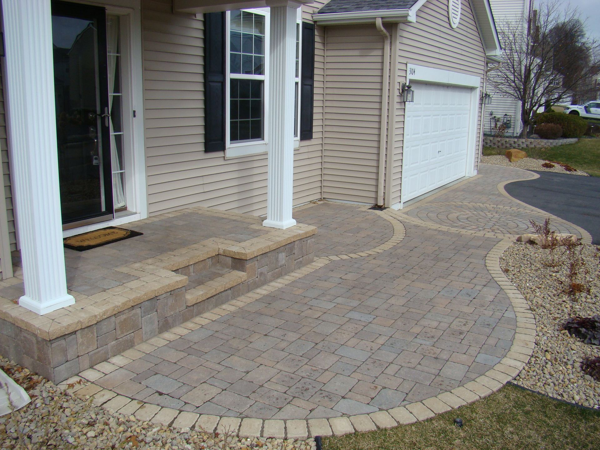 Brick walkway leading to a house with white pillars, beige siding, and a garage.