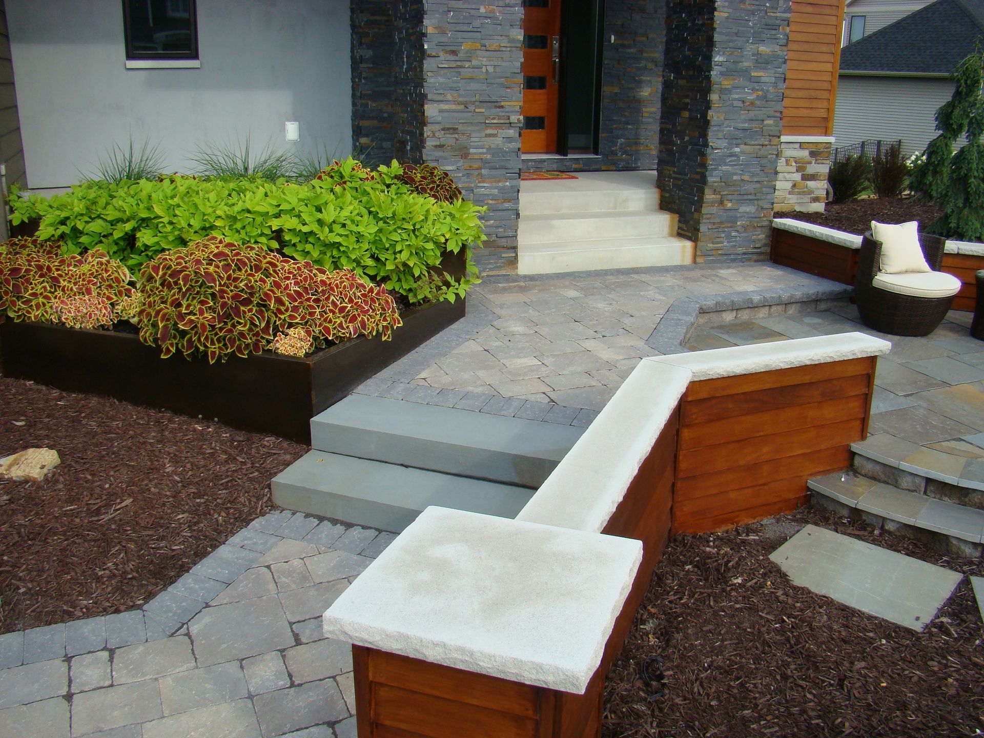 Modern home entrance with stone steps, wooden planters, and stone walkway.