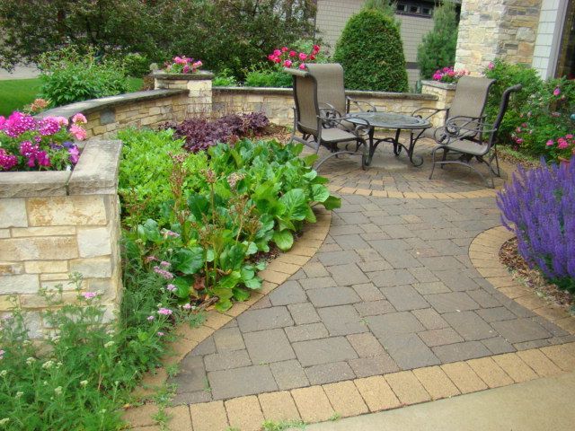 Stone patio with seating area, surrounded by flower beds and low stone walls.