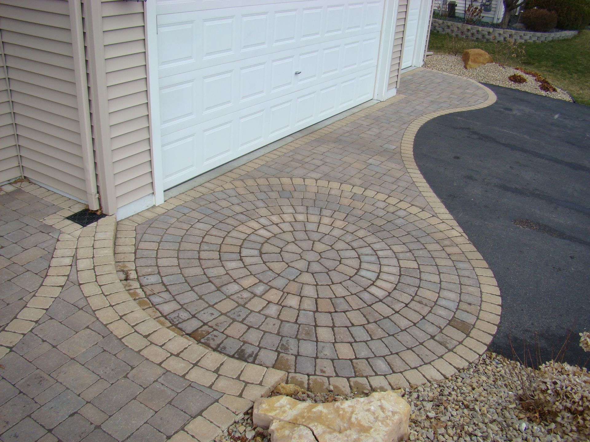 Brick walkway with circular and curved patterns leading to a garage door.