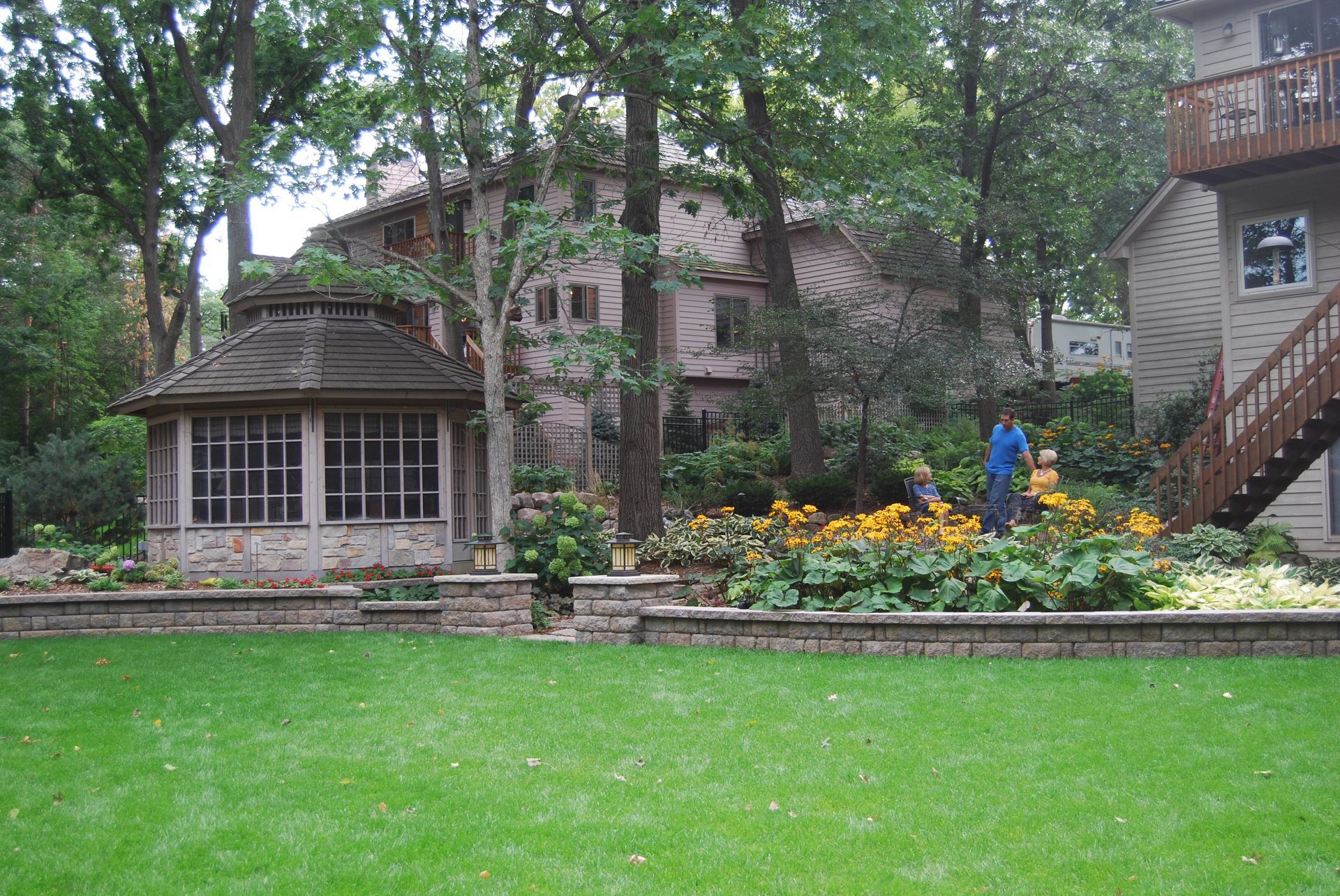 House with gazebo, garden, and person tending plants on a lawn.